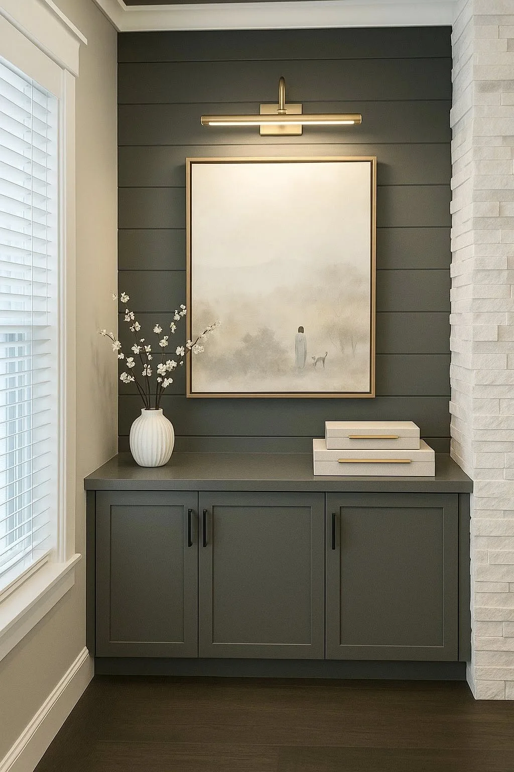 A dark gray sideboard with three cabinet doors, a white vase with white flowers, a large framed artwork, and two stacked white boxes with gold handles. Camp Renovation and Design in Columbus, Ohio.