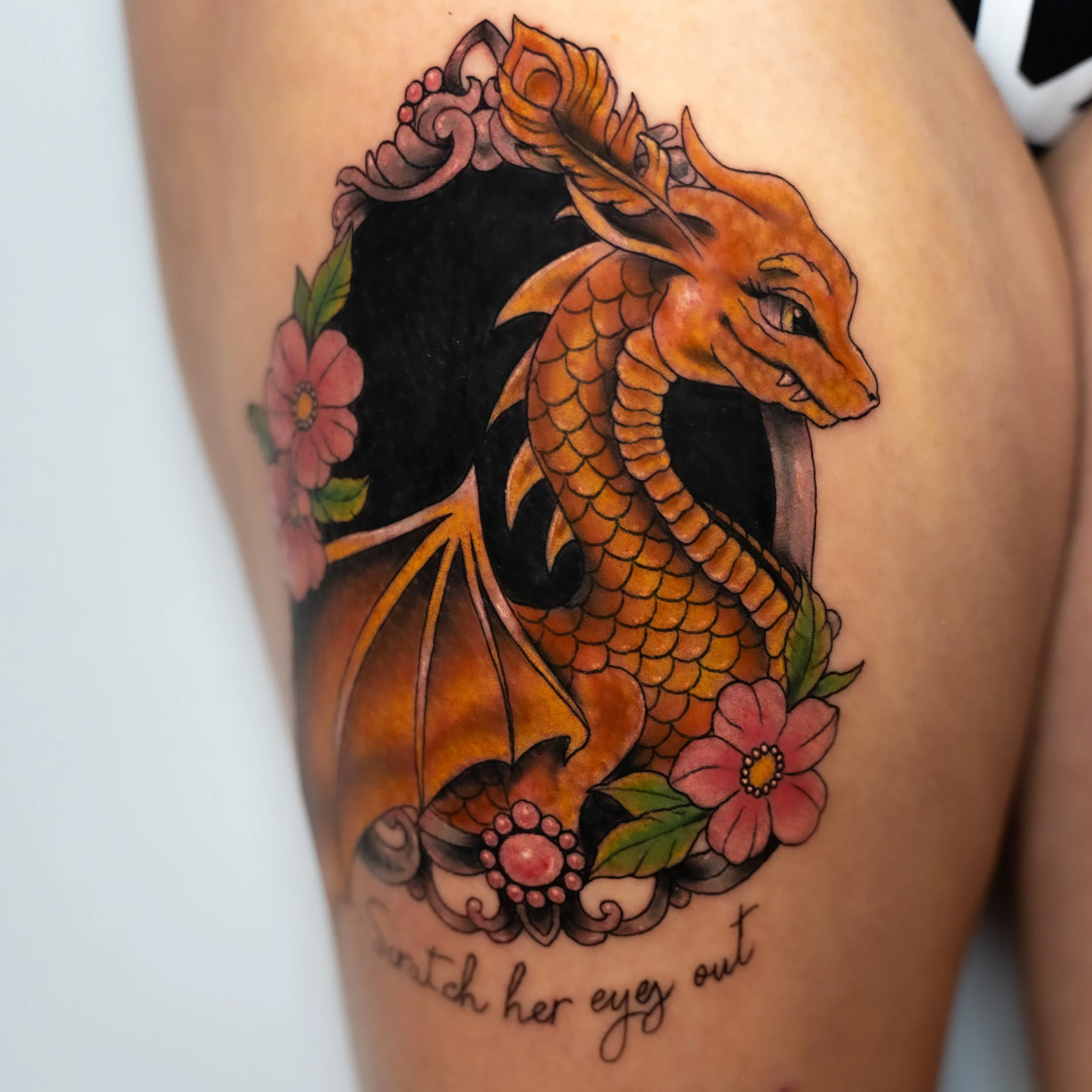 Colorful tattoo of a dragon with flowers and a quote.