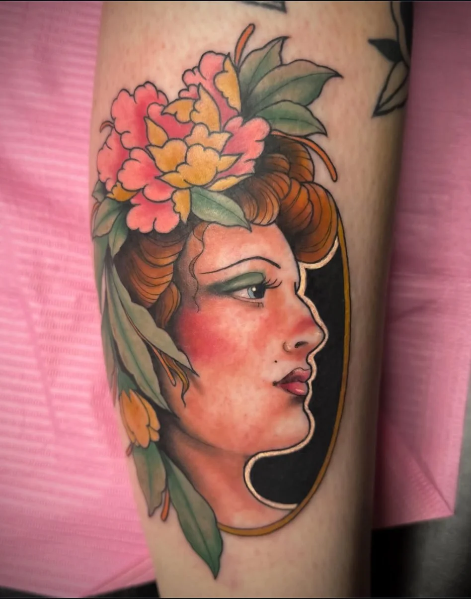 Tattoo of a woman's profile with flowers and leaves on her head, in a colorful, traditional style.