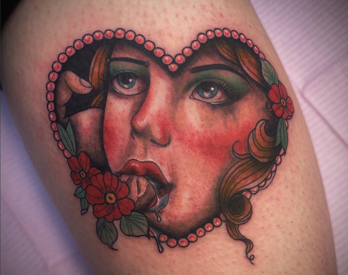 Tattoo of a woman's face with blue eyes, red lips, and flowing brown hair, surrounded by red flowers and a pearl necklace design.