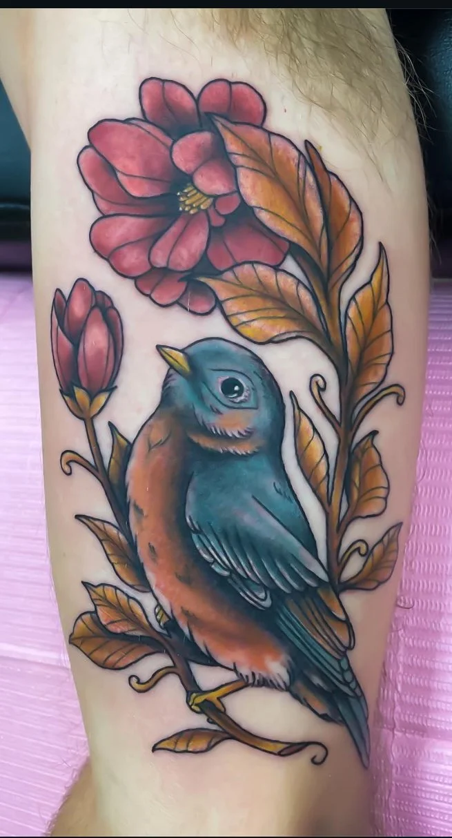 Tattoo of a colorful bird perched on a branch surrounded by red and orange leaves and flowers.
