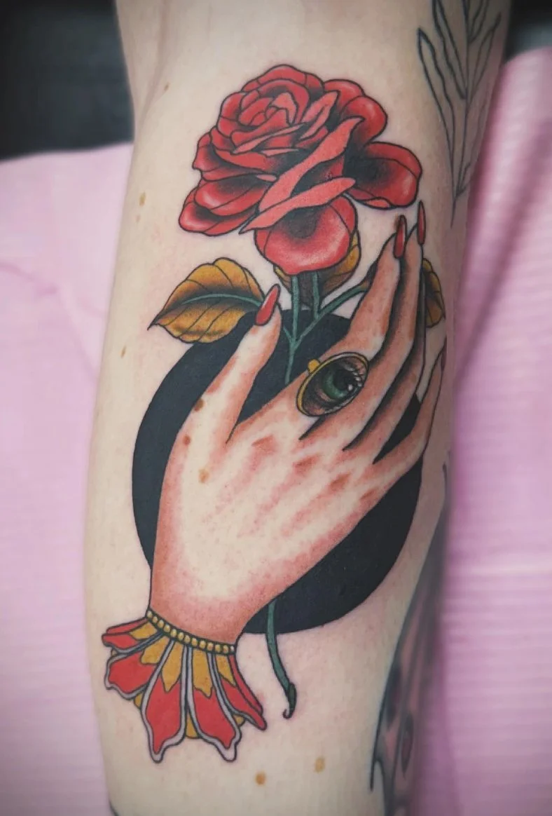 Tattoo of Anathama’s hand with red painted nails holding a red rose, wearing a large ring with a Jurian’s eye. Inspired by ACOTAR.