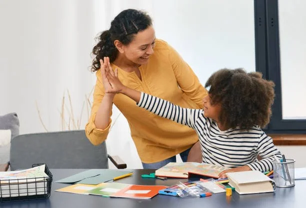 A woman and young girl with curly hair giving each other a high five at a table filled with school supplies.
