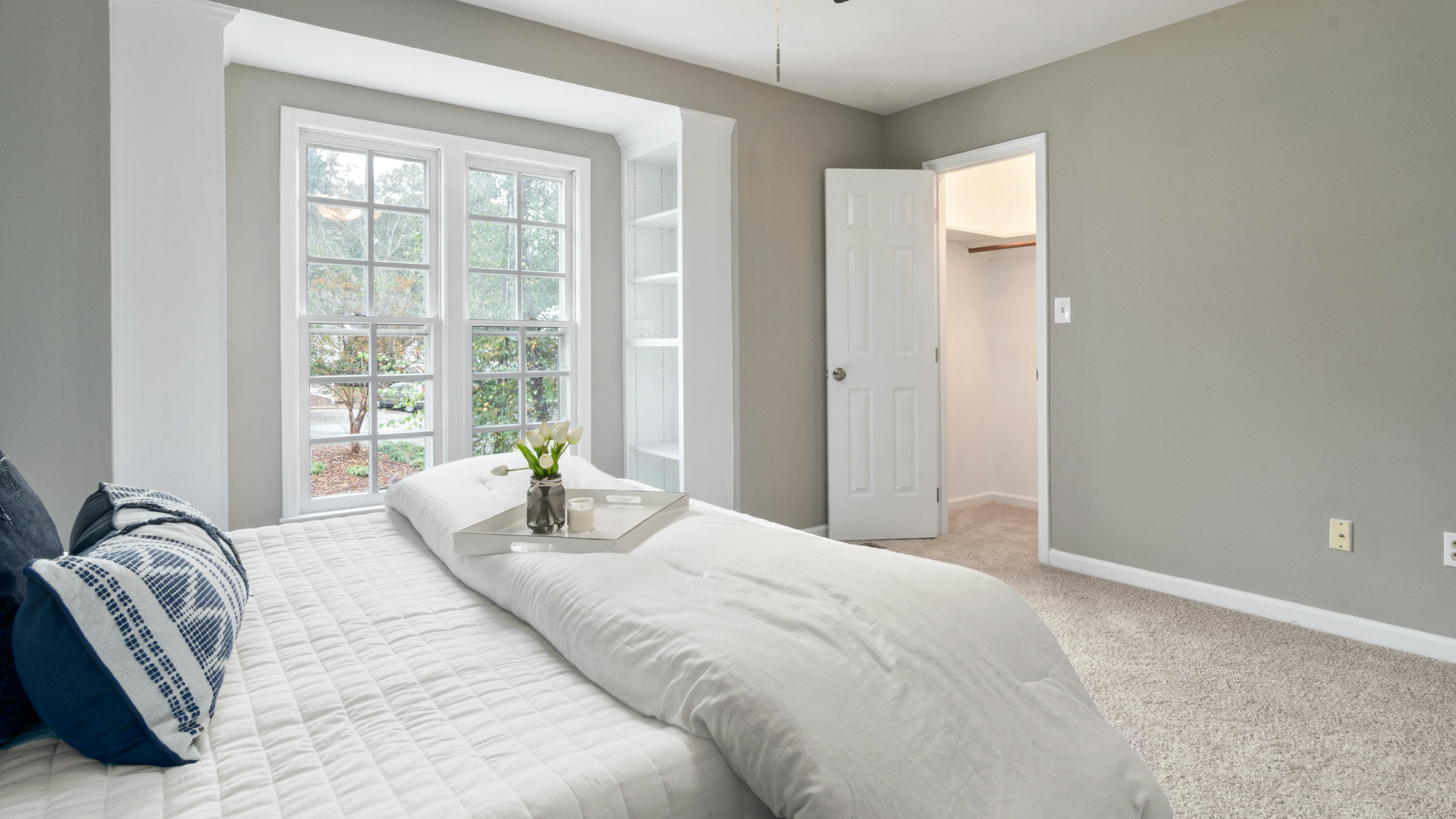 A bedroom with a large window, a bed with decorative pillows, and a closet with an open door.