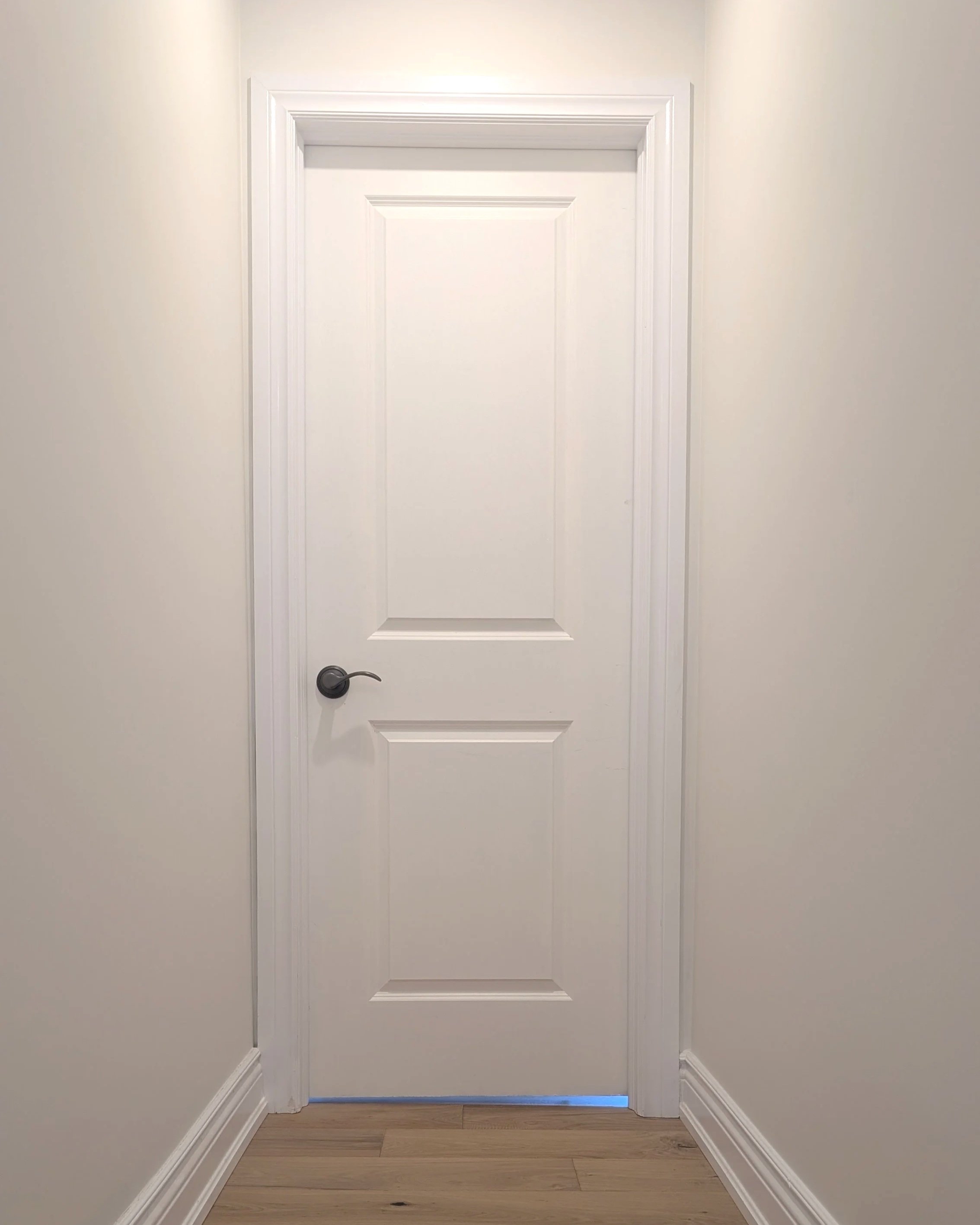 A white indoor door with black handle in a room with white walls and wood flooring. hardwood, lvp. slab door, painted, paint