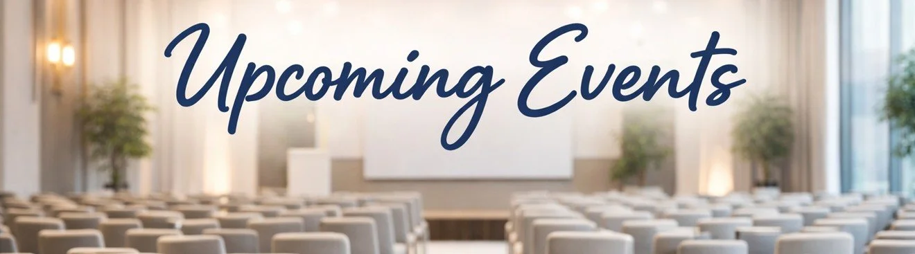 A conference room with rows of chairs facing a stage with a large screen, yellow carpeting, and outdoor lighting