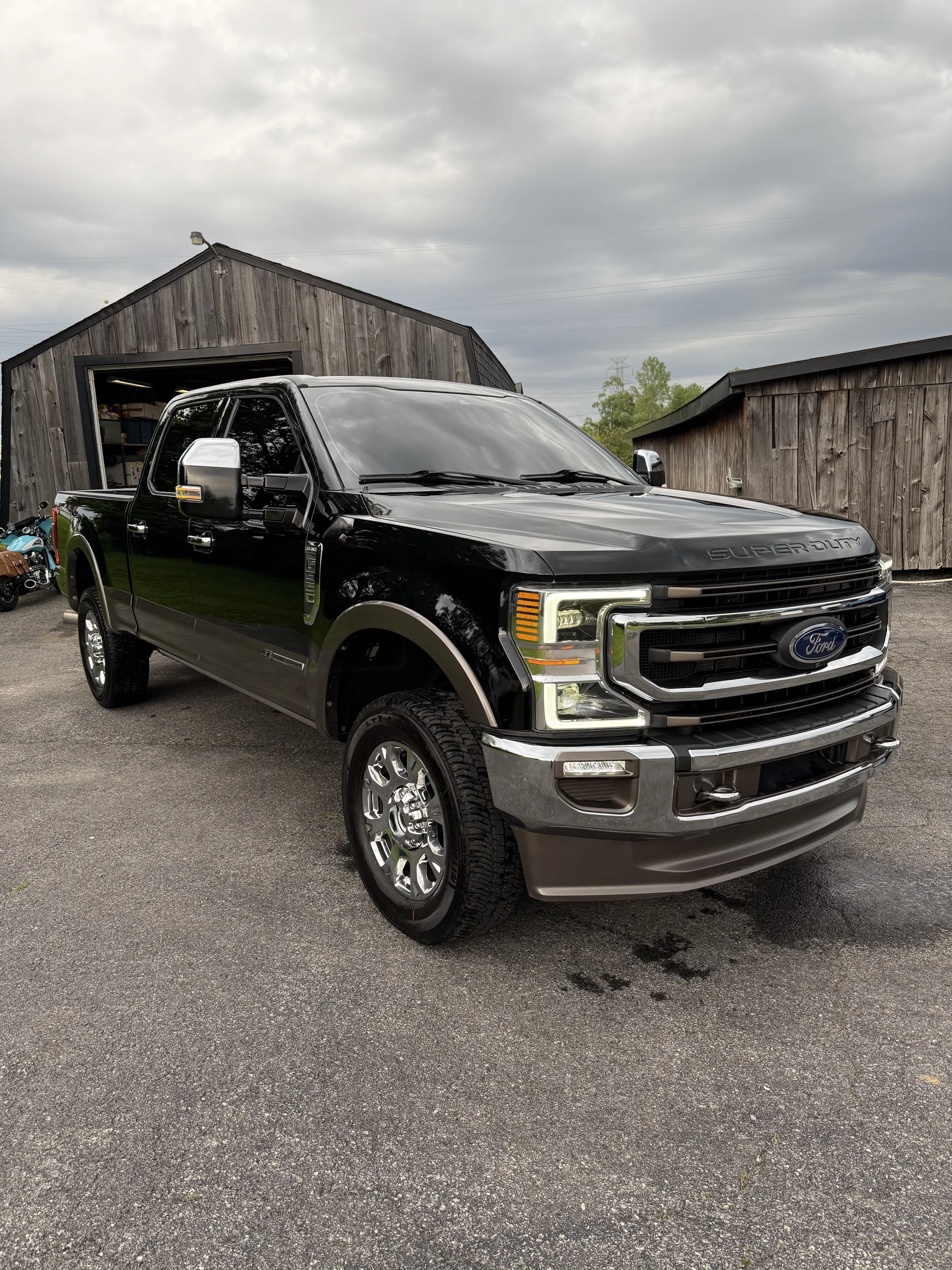 Black Ford Super Duty pickup truck parked on a paved lot with wooden buildings in the background.