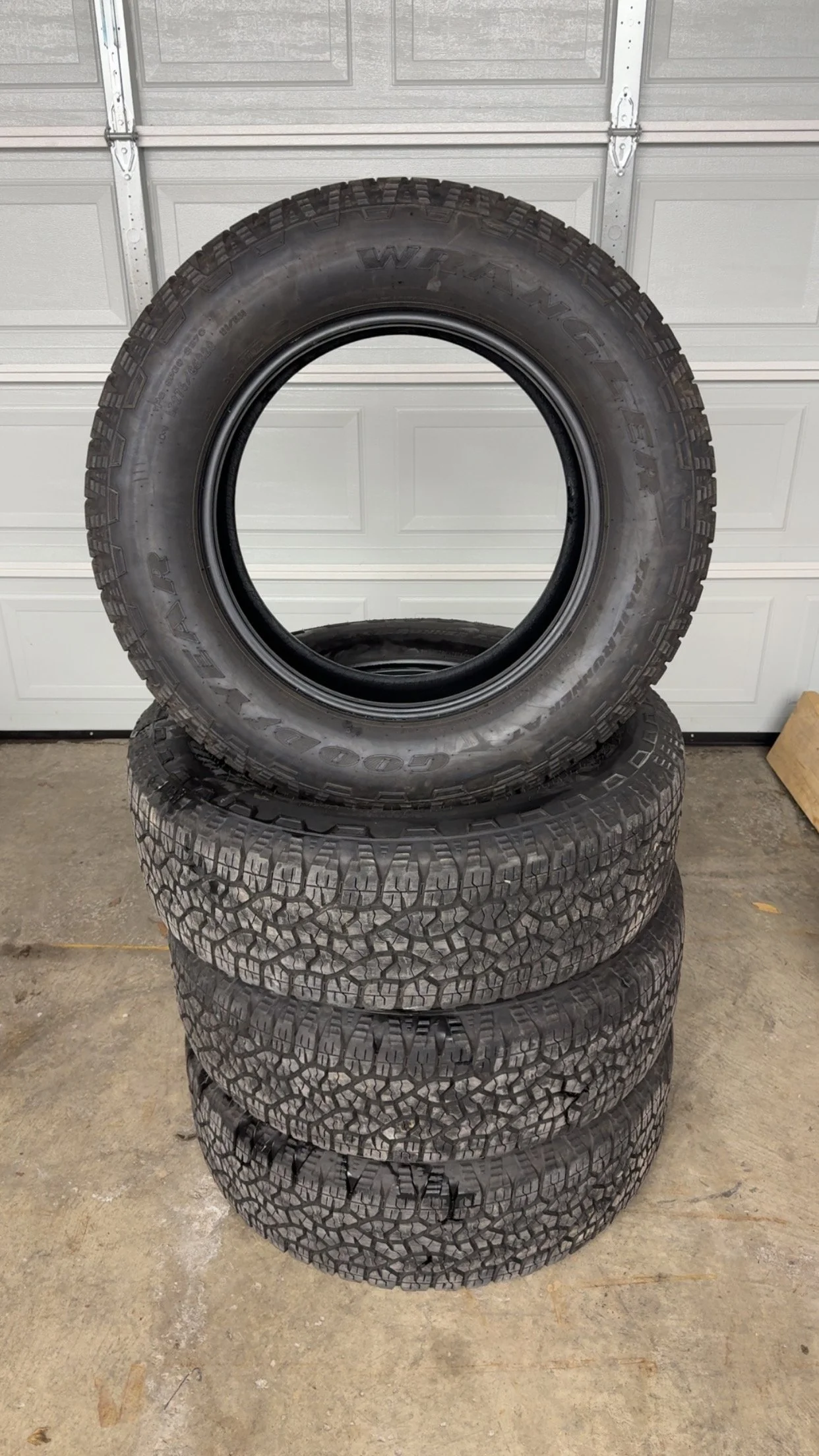 Four stacked tires, with one tire standing upright on top of three tires with worn tread in a garage.
