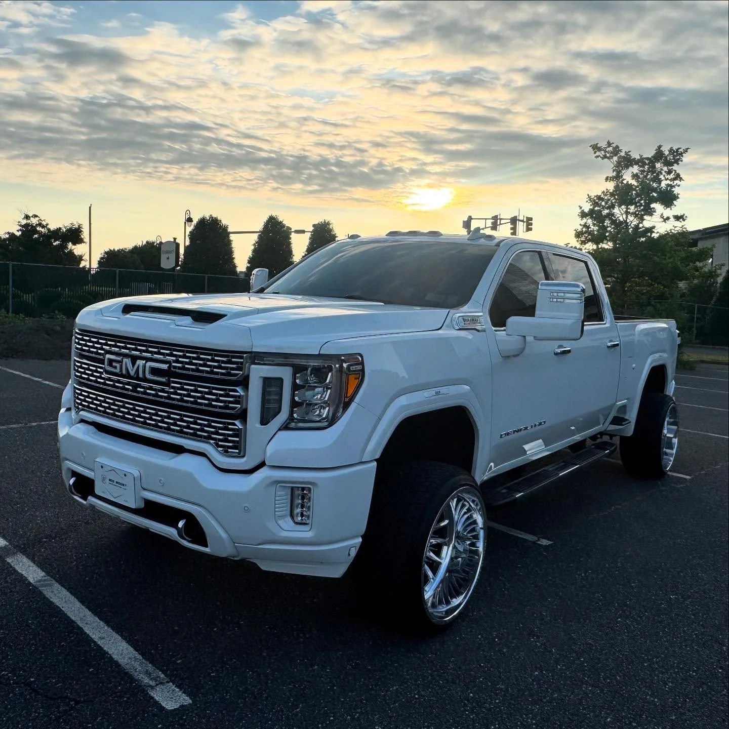 A white GMC pickup truck parked in a lot at sunset, with large shiny rims, black tinted windows, and chrome accents.