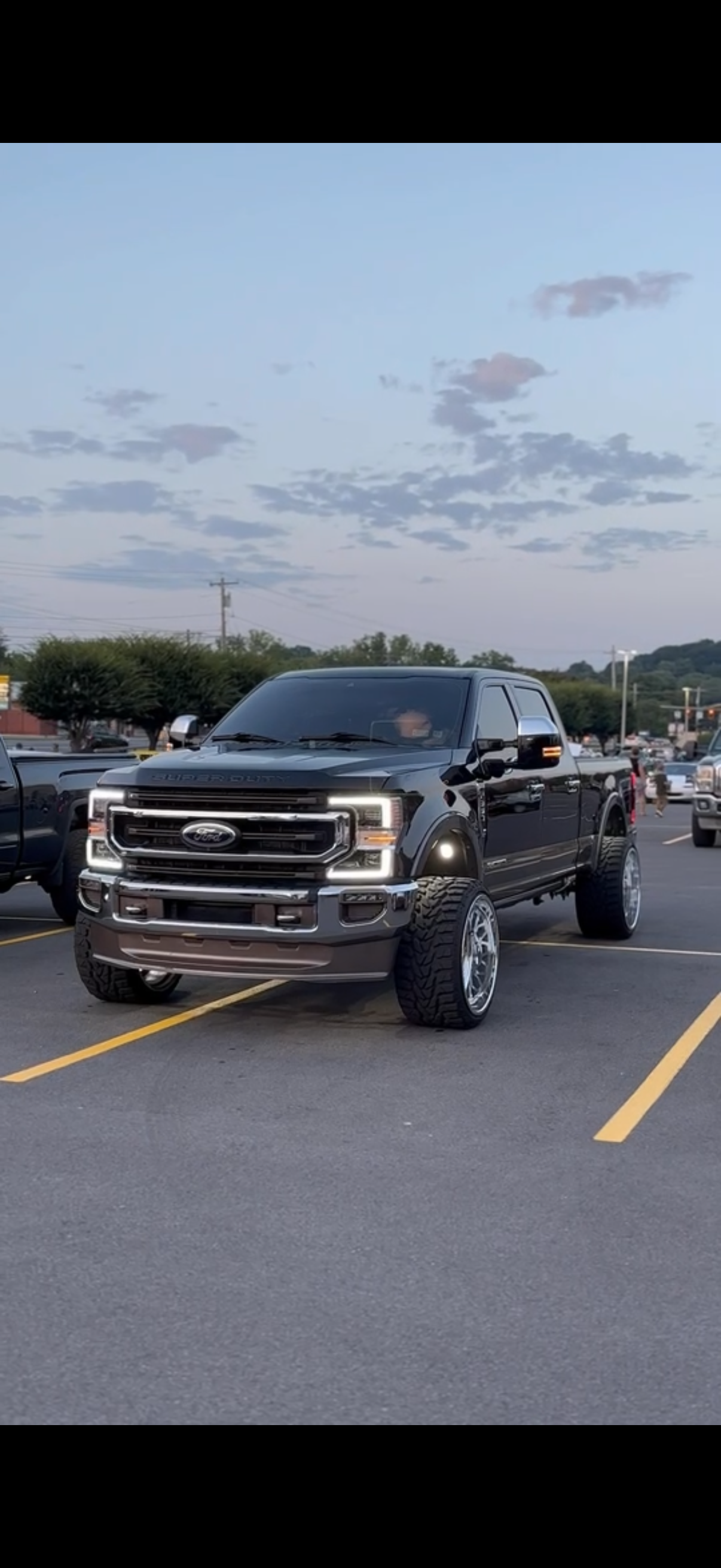 Black lifted Ford pickup truck parked in a parking lot during dusk with a partly cloudy sky.