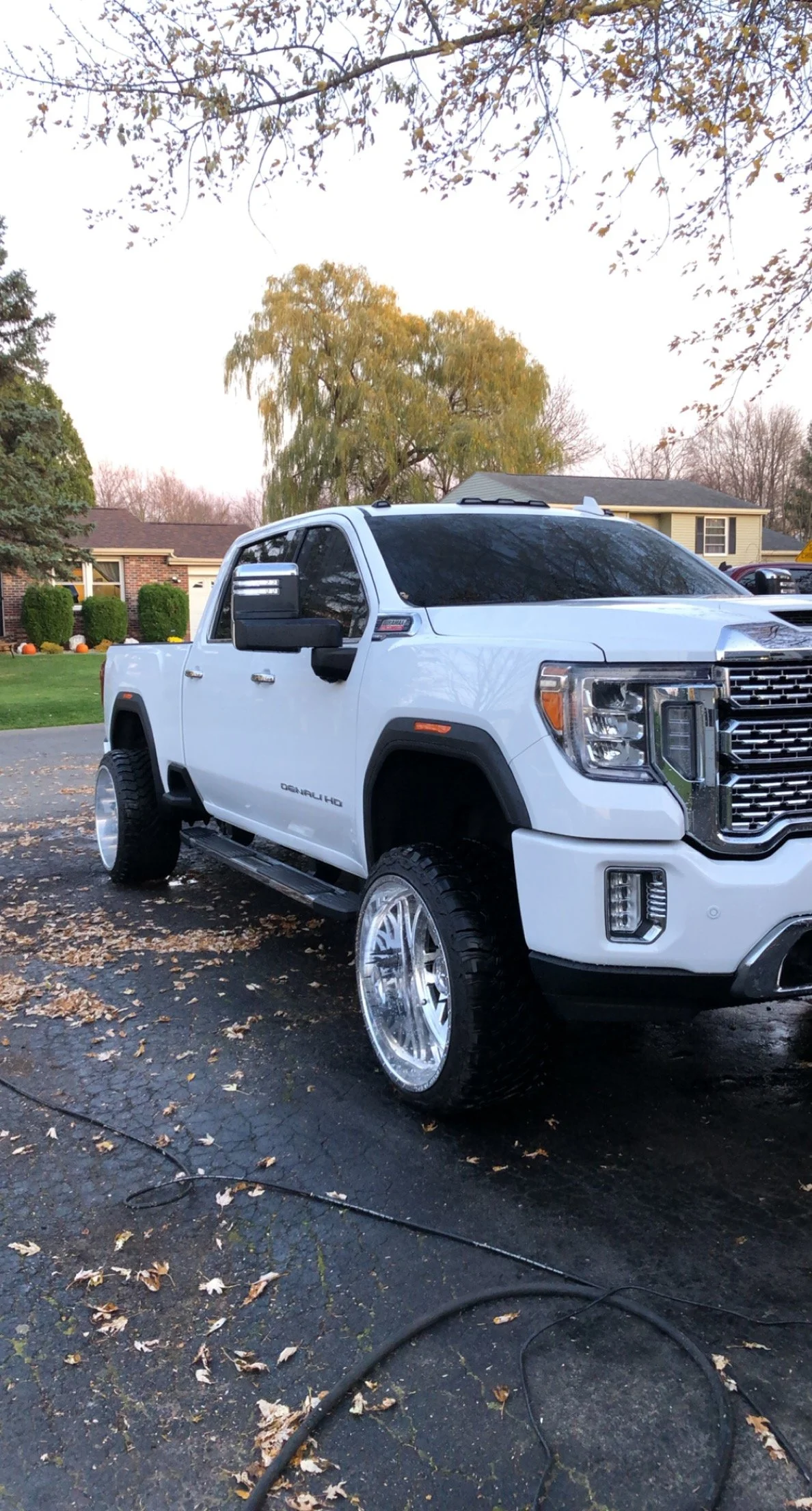 White pickup truck parked on driveway on an autumn day with fallen leaves, trees, and houses in the background.