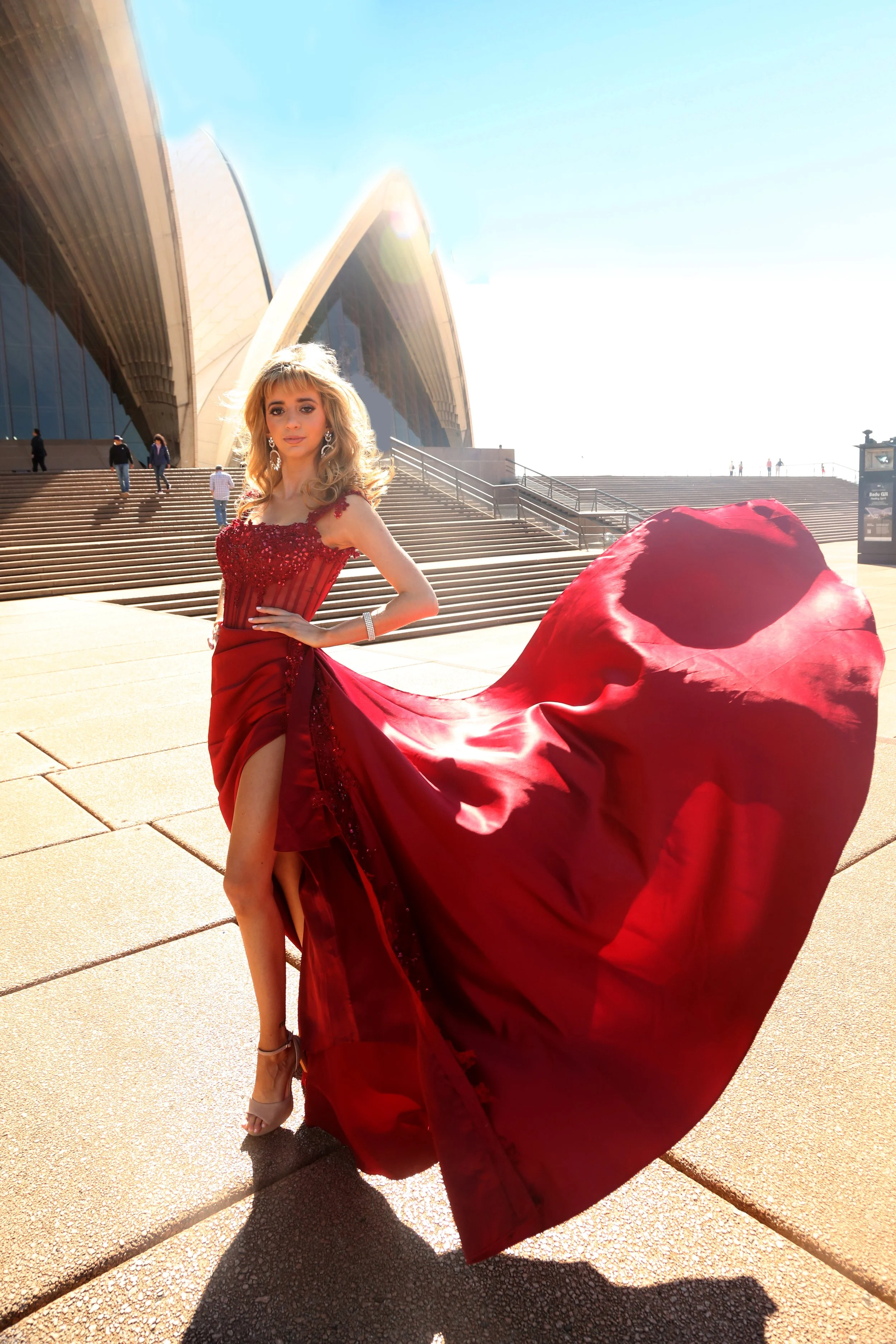 A woman in a red gown in front of the Sydney Opera House.