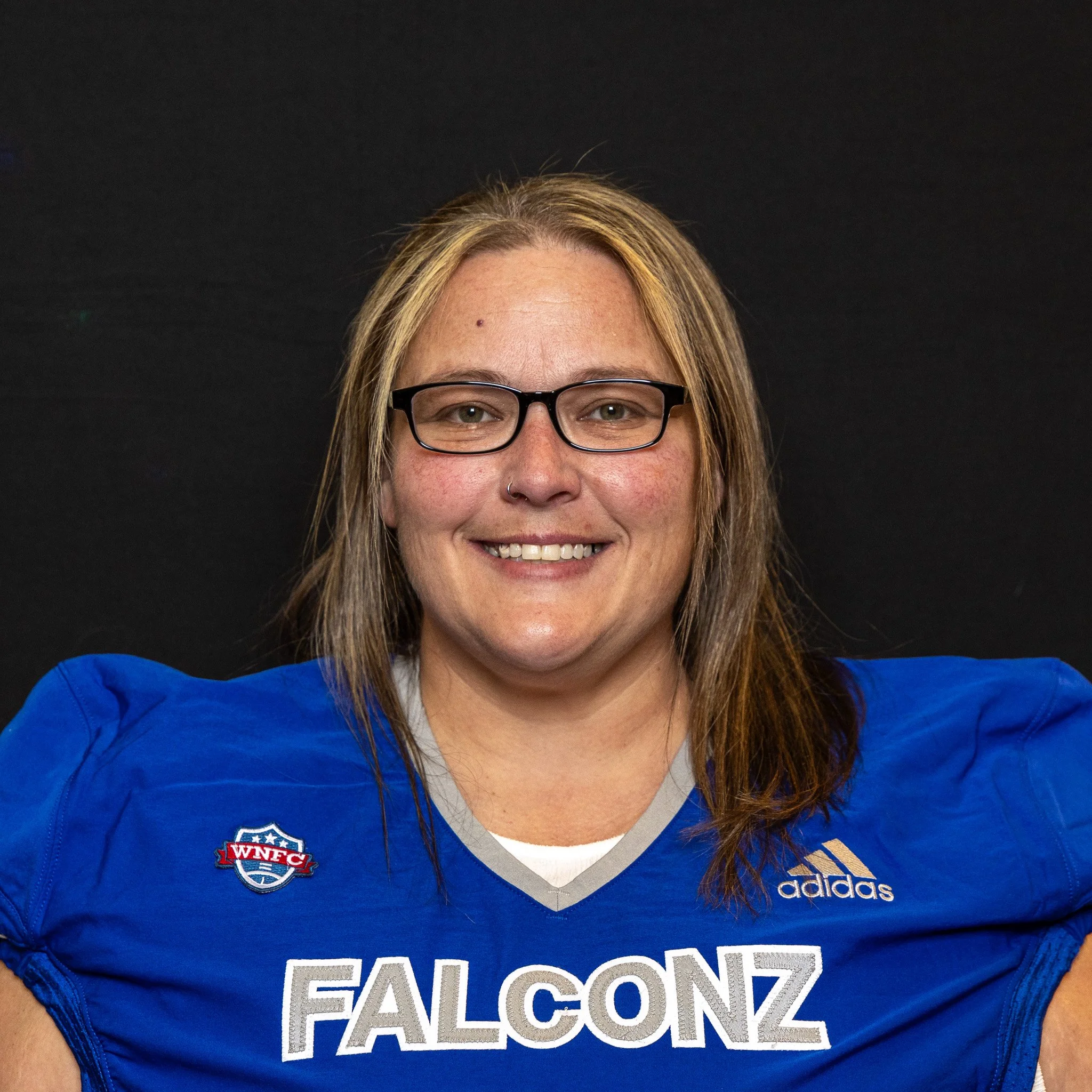 A woman wearing glasses and a blue football jersey with 'FALCONZ' written on it, smiling against a black background.