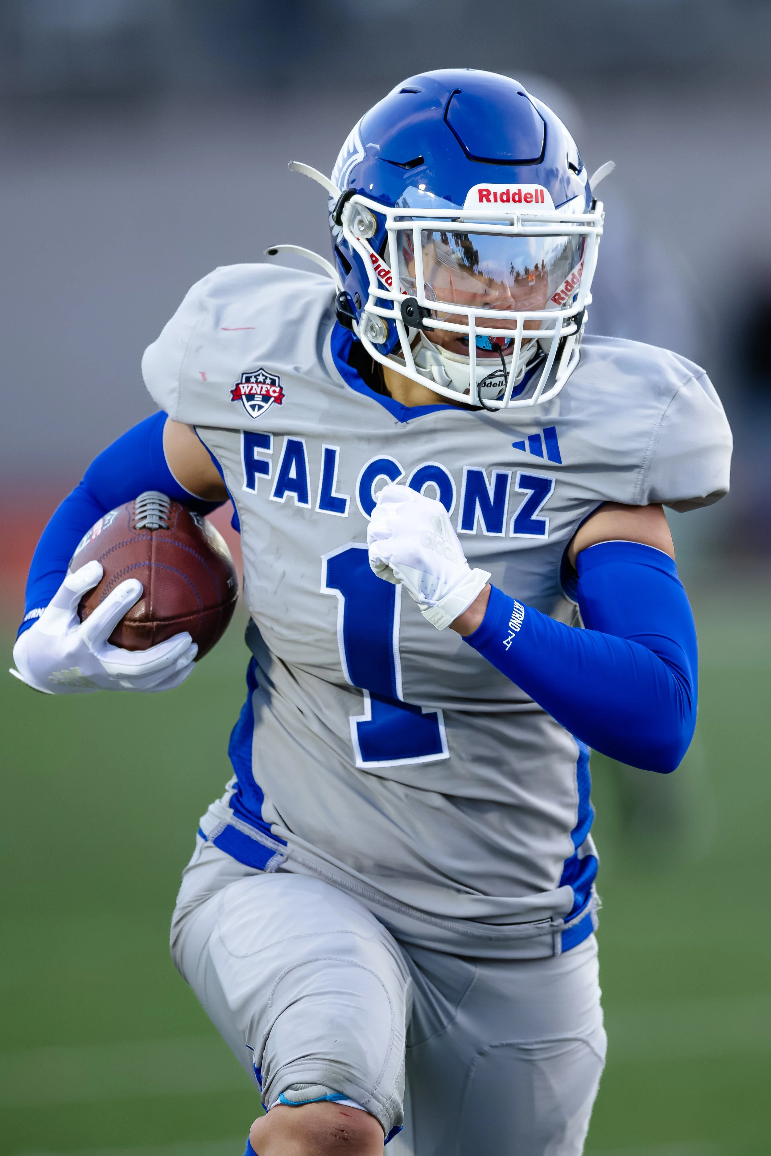 An American football player in a white and blue uniform holding a football, running on the field.