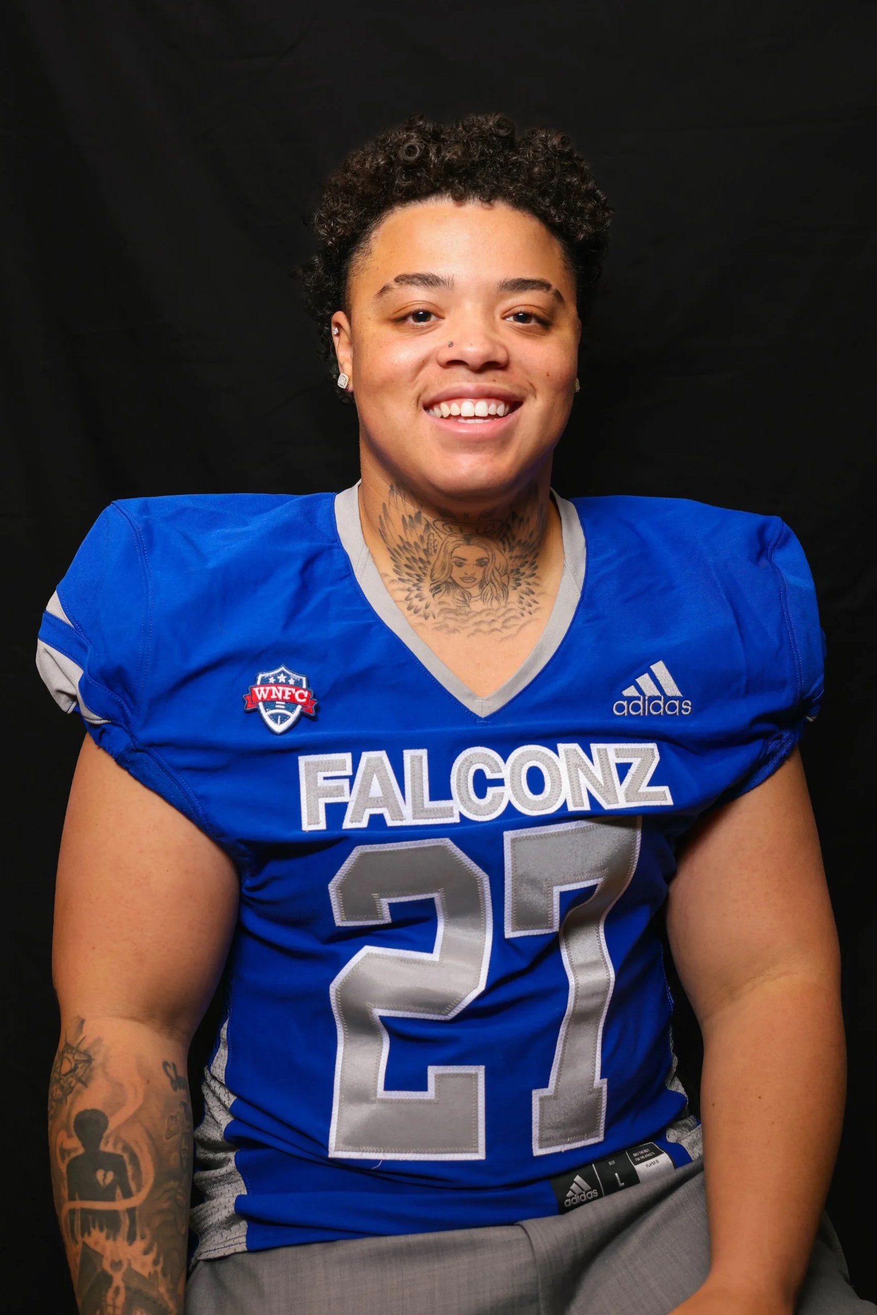 A woman wearing glasses and a blue football jersey with 'FALCONZ' written on it, smiling against a black background.