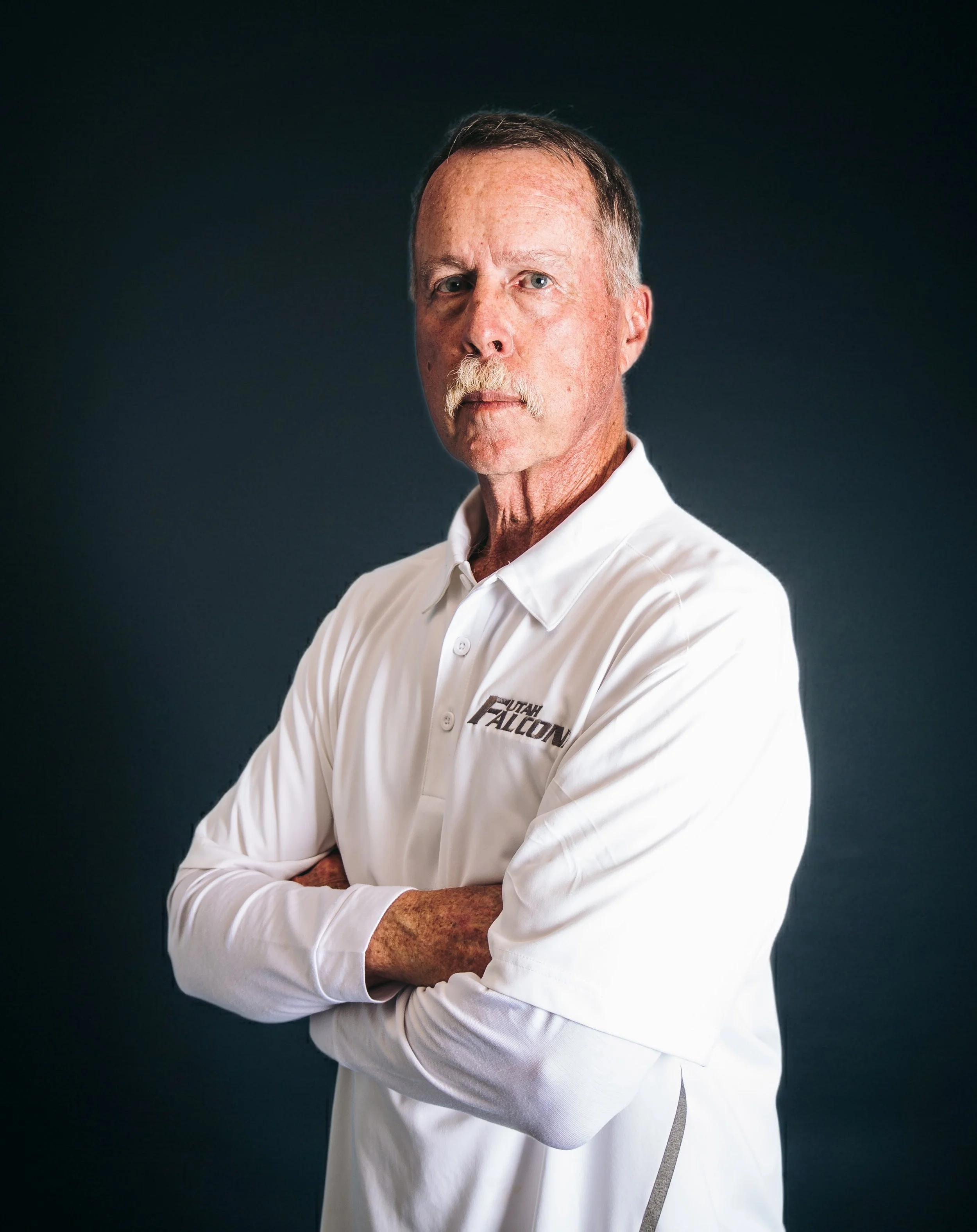 A portrait of a middle-aged man with short light brown hair, wearing a blue jacket, against a gradient dark background.
