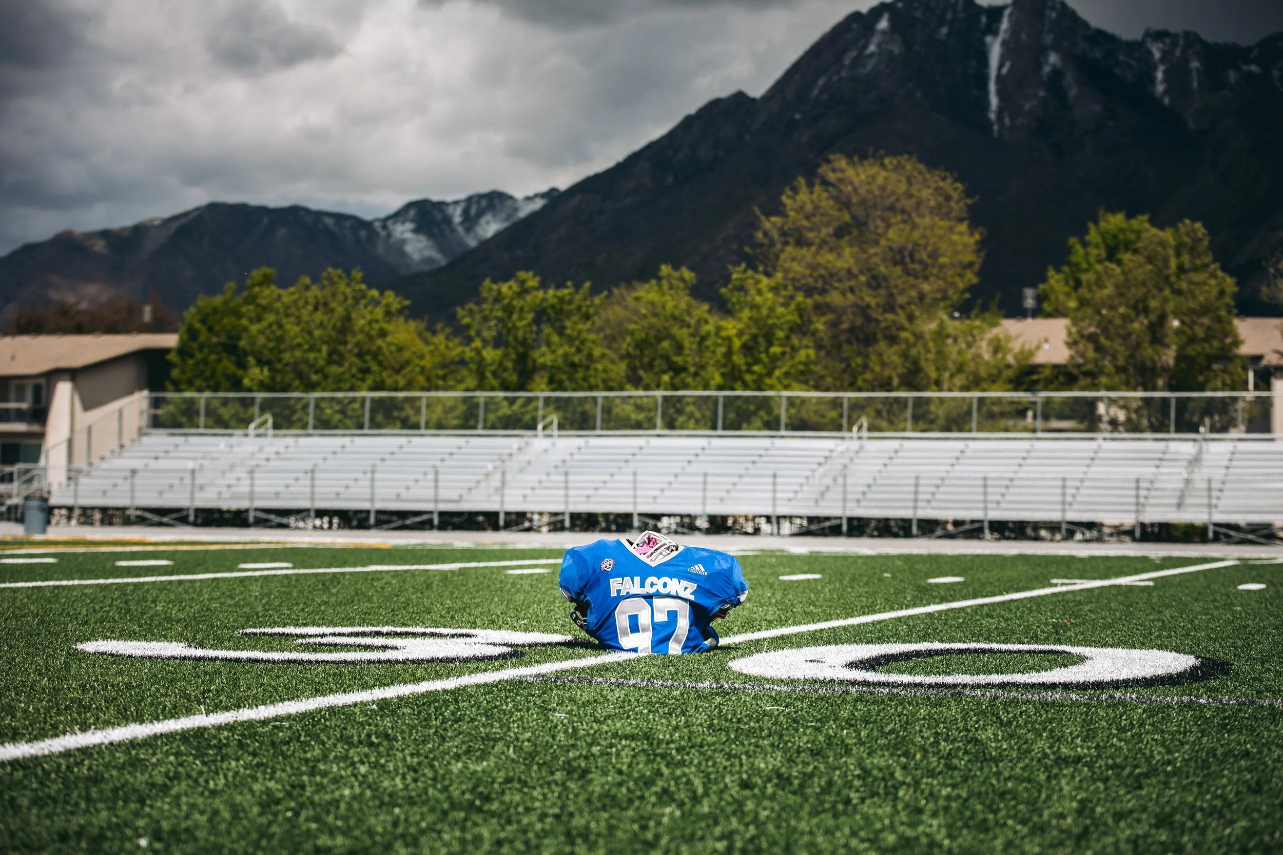 A football helmet and uniform are placed on a football field, with bleachers and mountains in the background.
