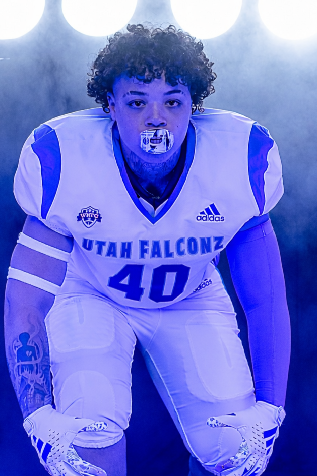 A woman wearing glasses and a blue football jersey with 'FALCONZ' written on it, smiling against a black background.