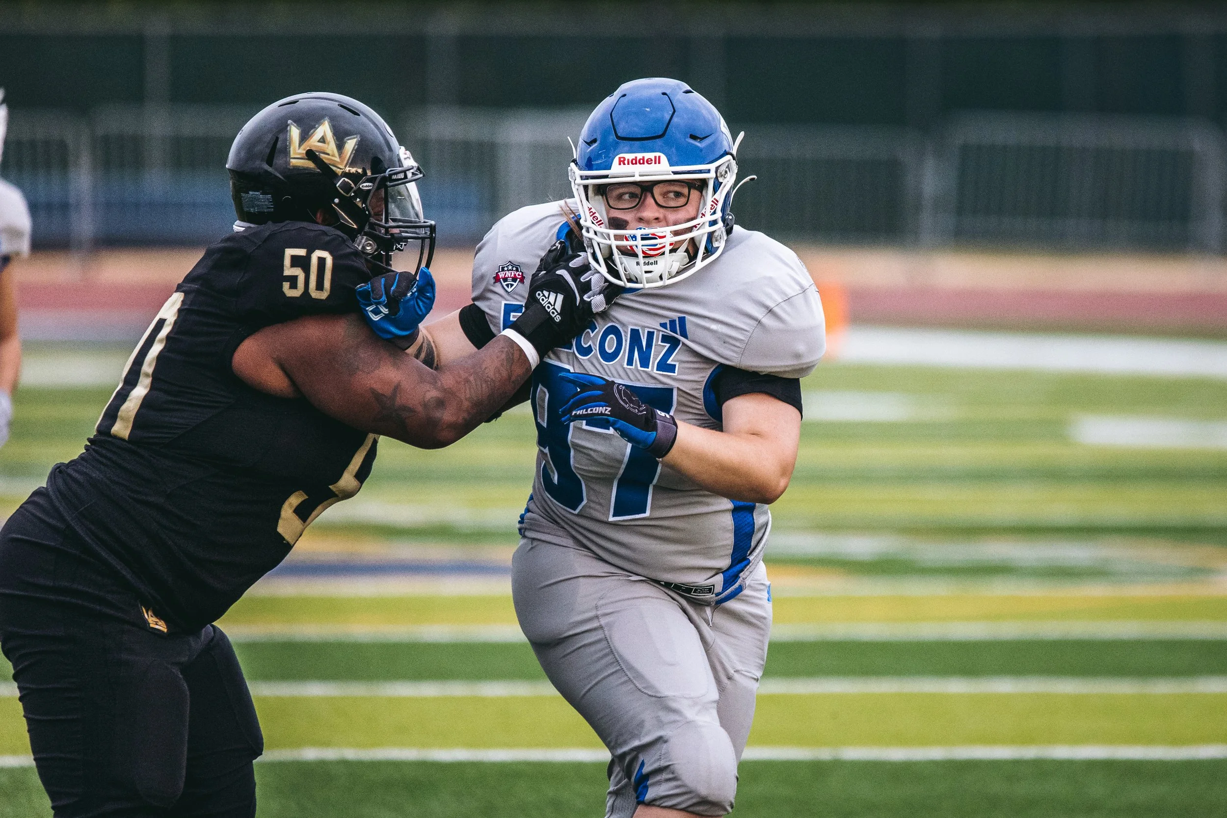 An American football player in a gray and blue uniform running while being tackled by a player in black and gold uniform.