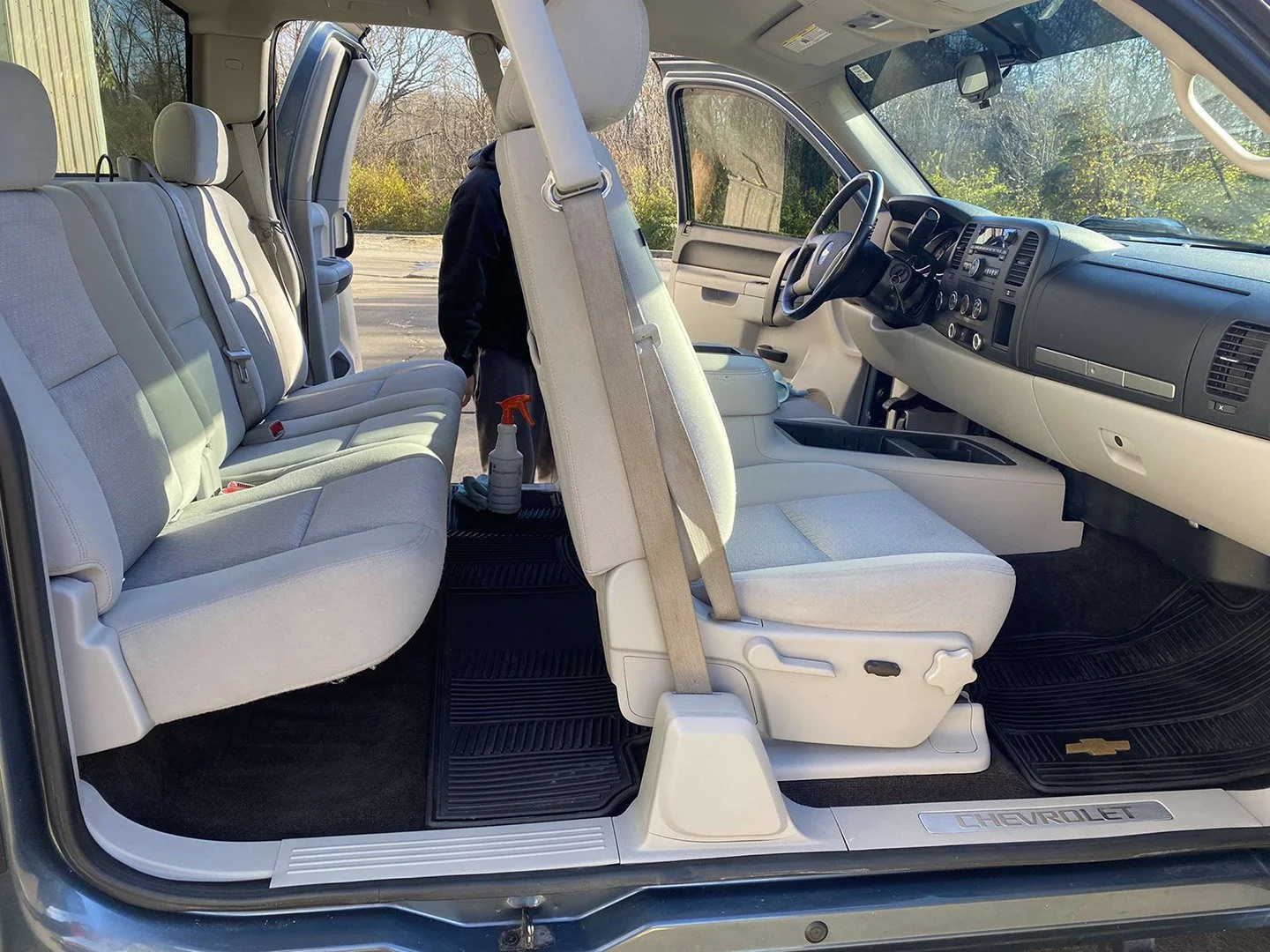 Interior of a Chevrolet van with light-colored seats, some seats folded up, and various cleaning supplies in the front area.