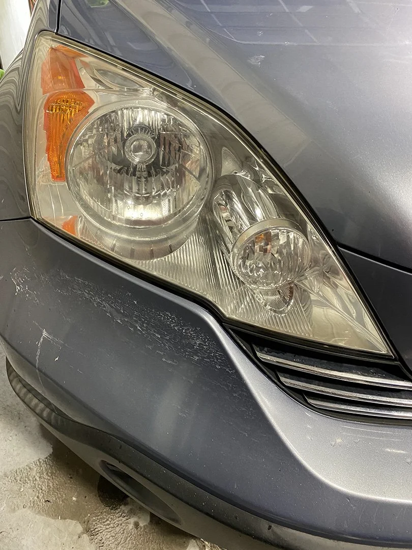Close-up of a gray car's front headlight and bumper, showing scratches and minor damage