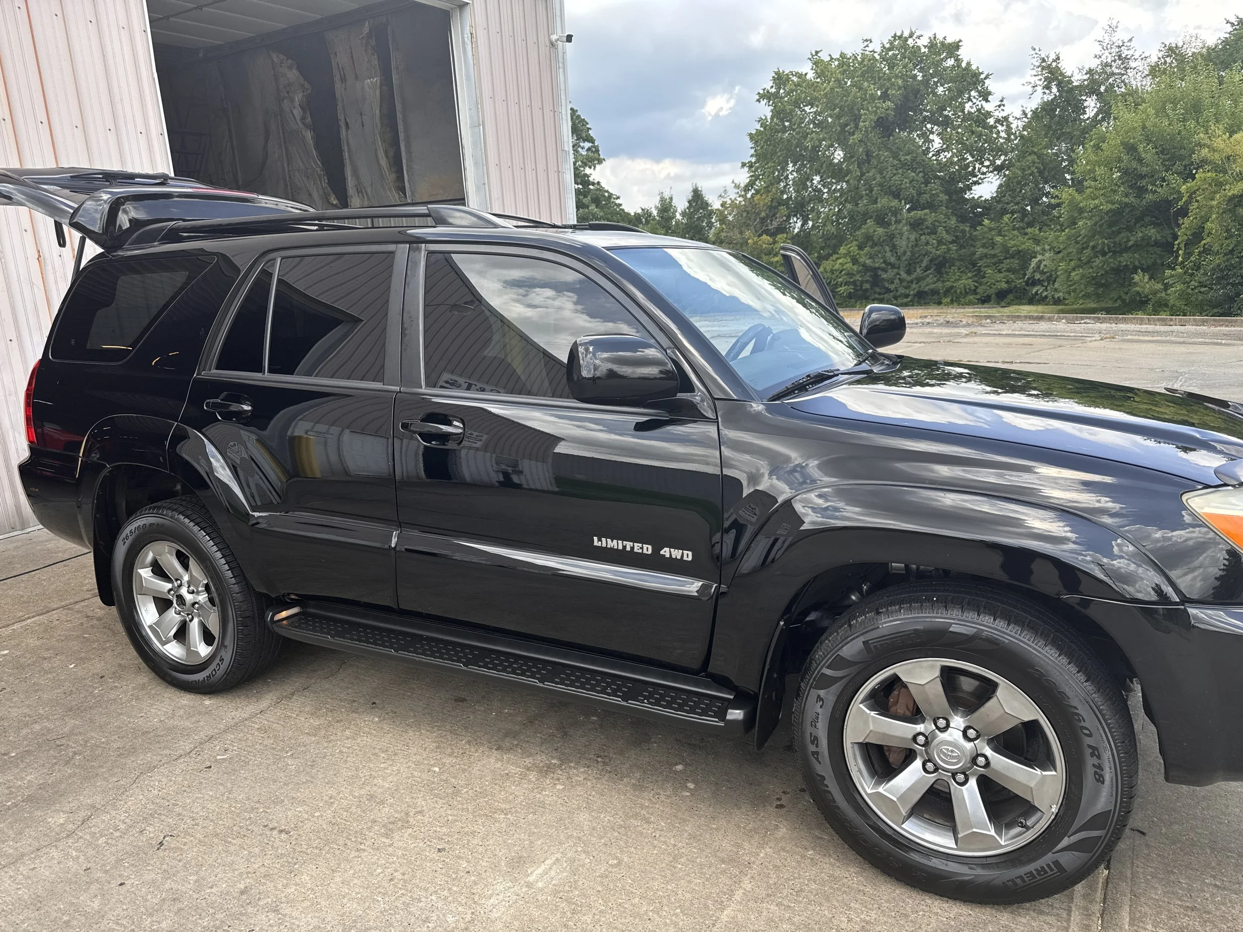 Black SUV parked outside near a building with trees in the background, with a sign near the front wheel reading "Limited 4WD."