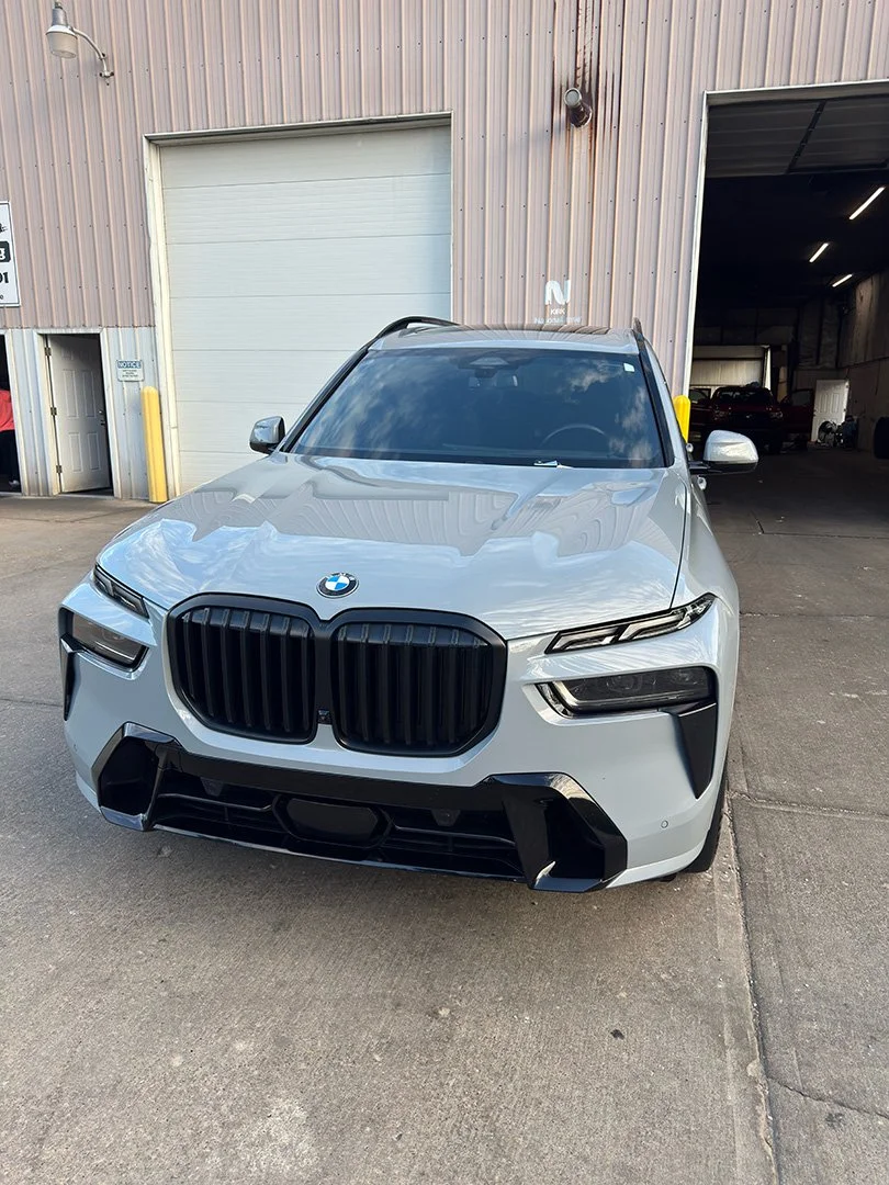 Front view of a silver BMW SUV parked outside a building with a garage door and a partially open door.