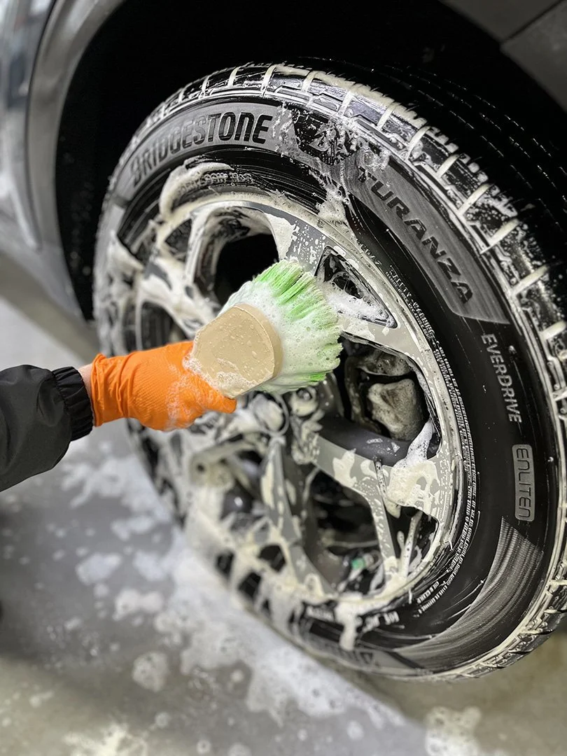 Person cleaning and scrubbing a car tire with soap and brush.