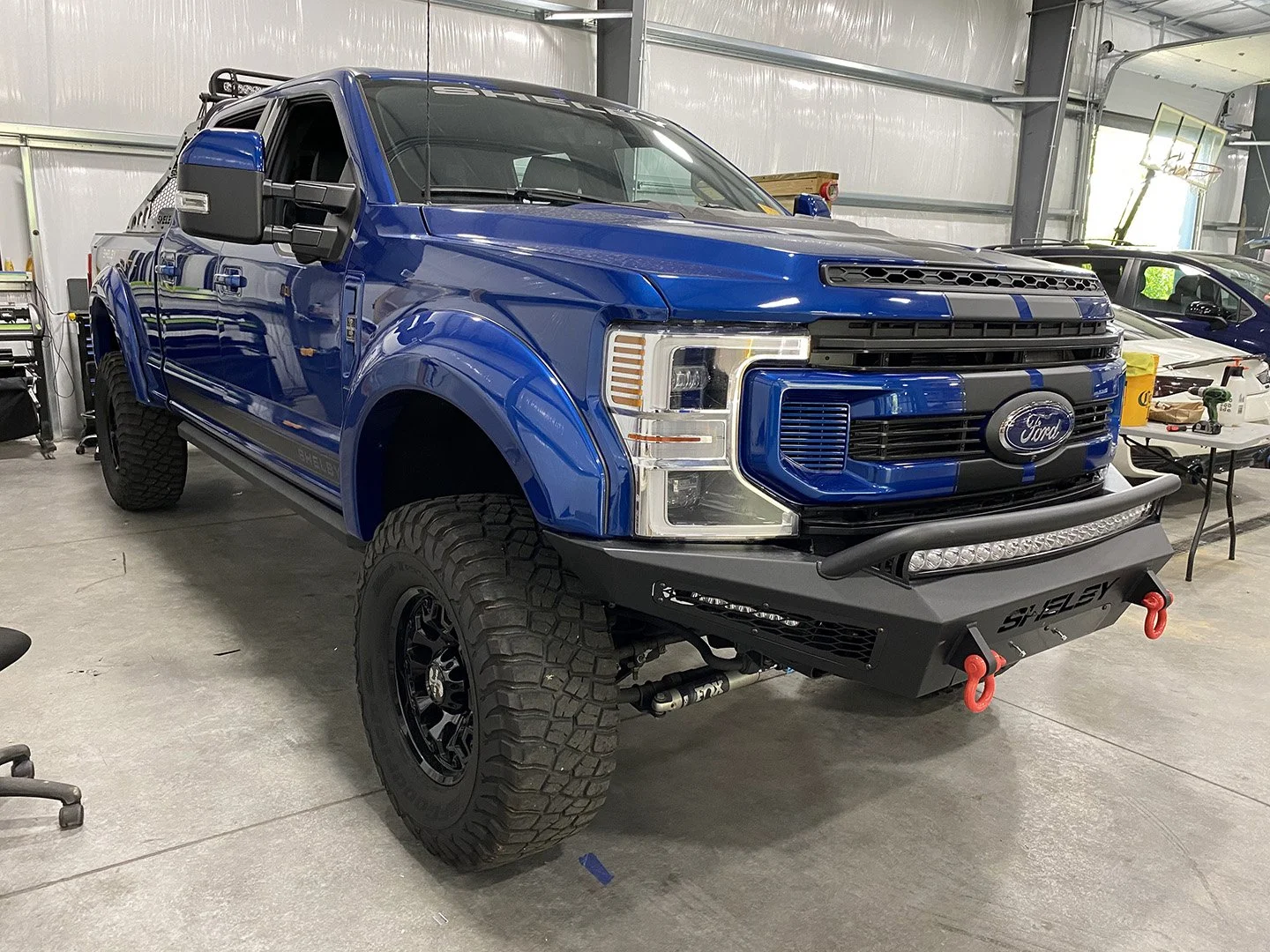 Blue Ford pickup truck with off-road modifications inside a garage or workshop.