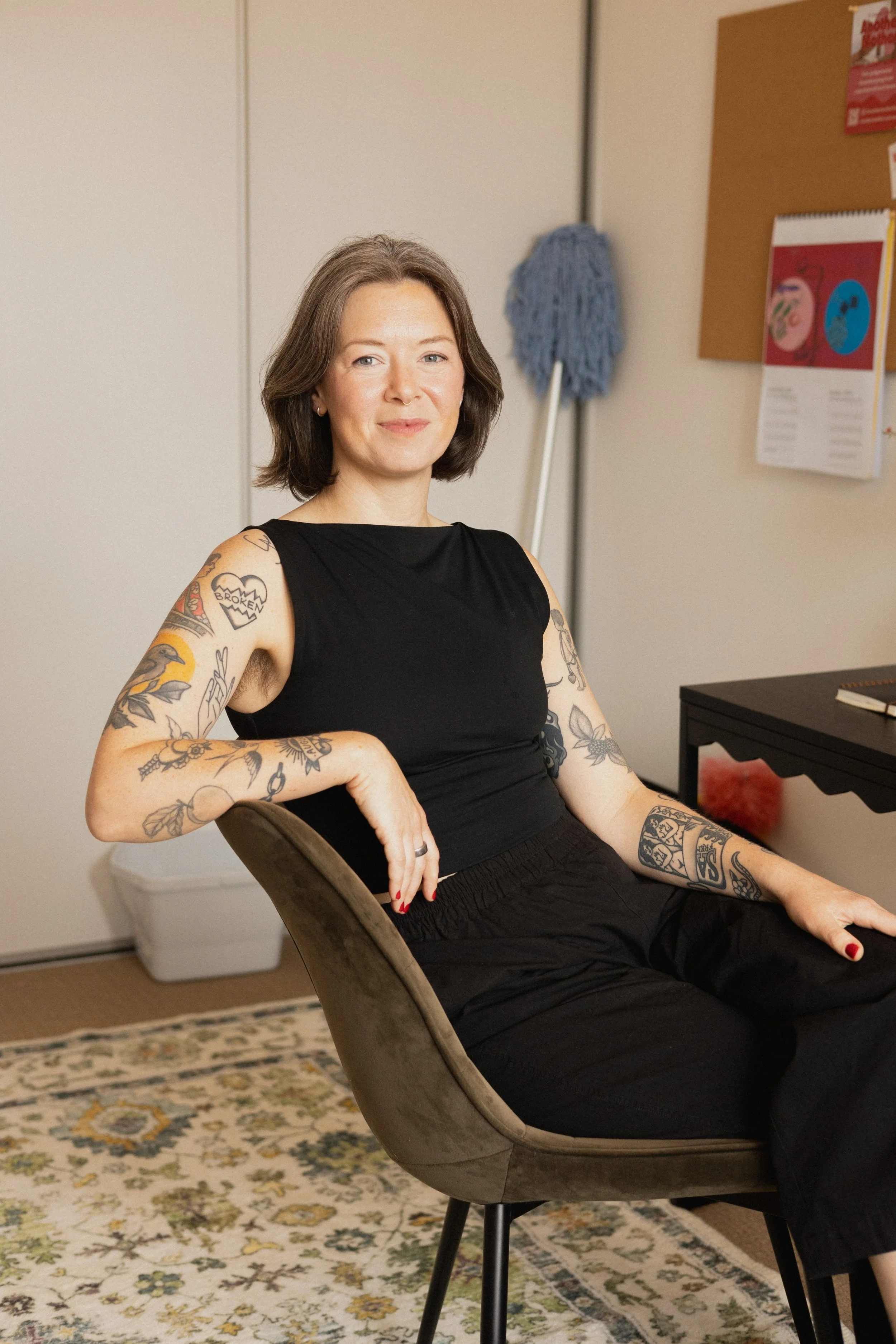 The founder of Another Mother sits in a home office, smiling warmly while seated at a desk, reflecting the supportive, non-judgemental housekeeping values behind the Perth-based service.