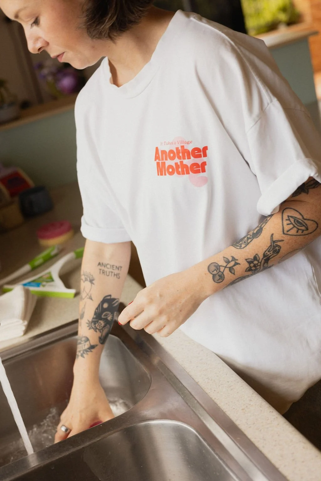 A housekeeper from Another Mother wipes down a kitchen bench and stainless steel sink, demonstrating the practical, non-judgemental housekeeping services offered to Perth families.