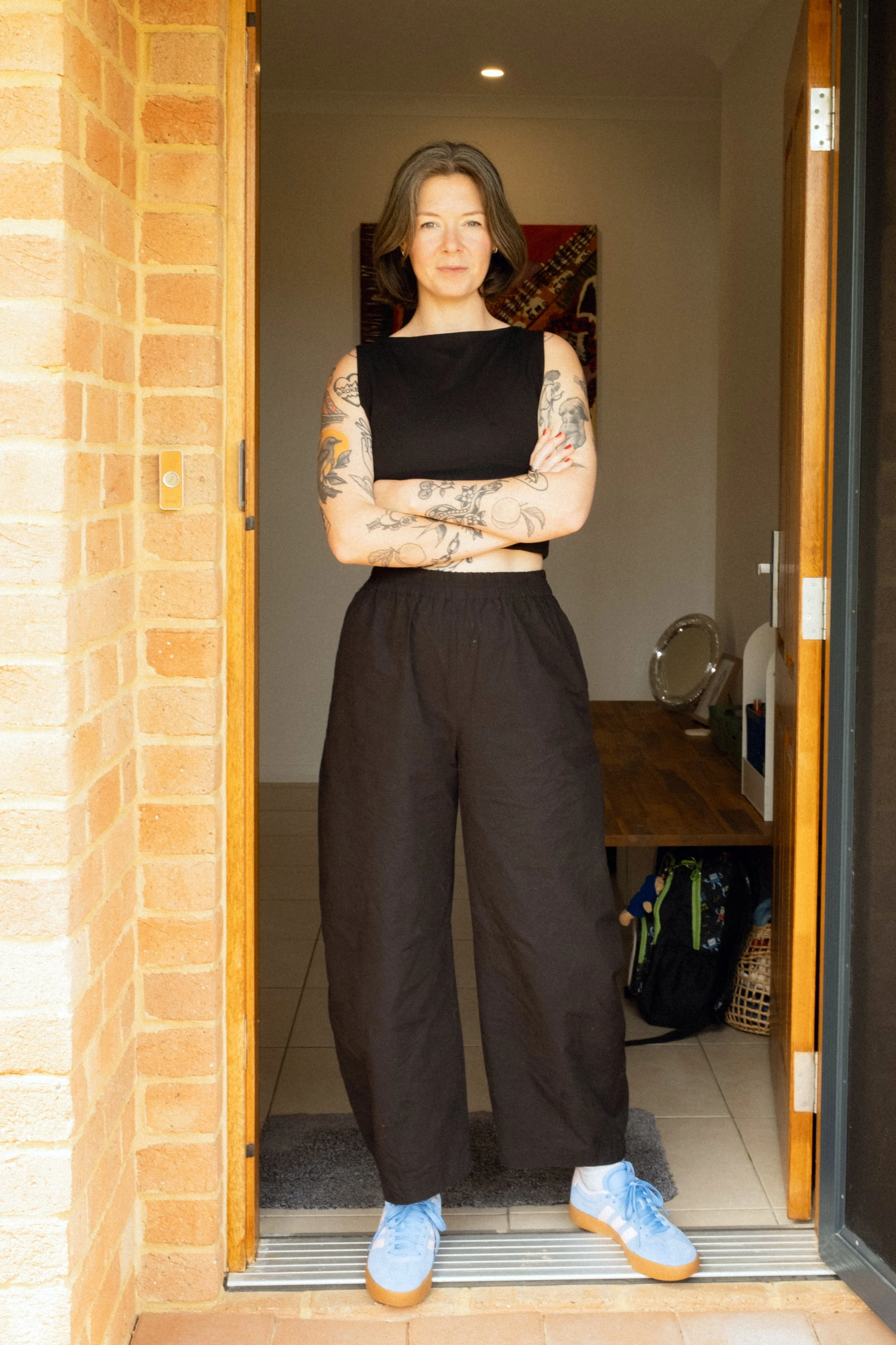 Hannah Purvey-Tyrer, founder of Another Mother, stands confidently in a doorway of a Perth home with arms crossed, representing non-judgemental housekeeping and practical support for mums.