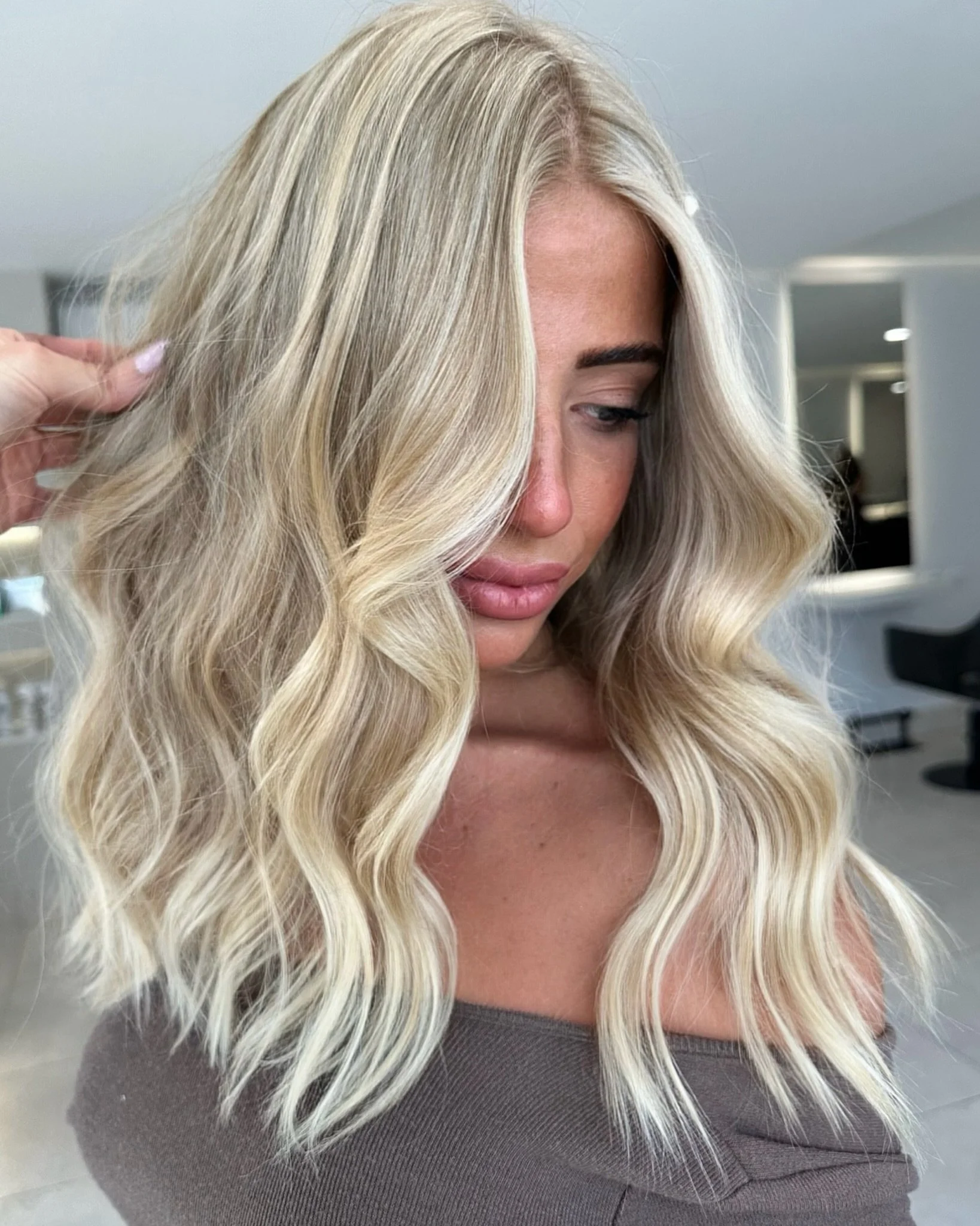 Woman with long, wavy blonde hair being styled in a hair salon.