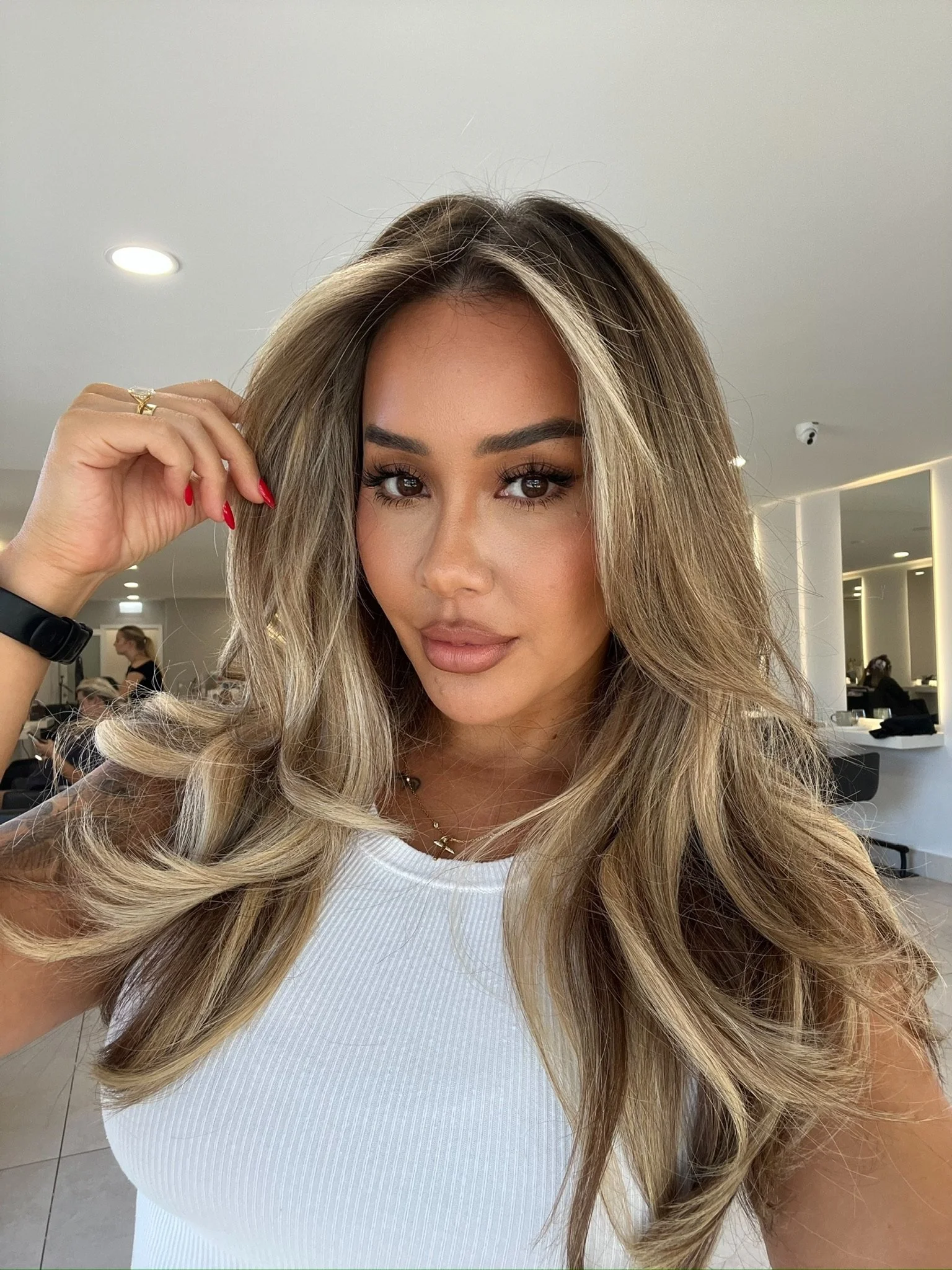 A woman with long, wavy blonde hair taking a selfie in a modern, well-lit indoor space.