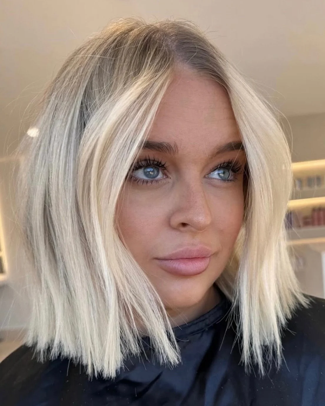 Close-up of a woman with platinum blonde, shoulder-length hair, blue eyes, and full lips, looking slightly upwards.