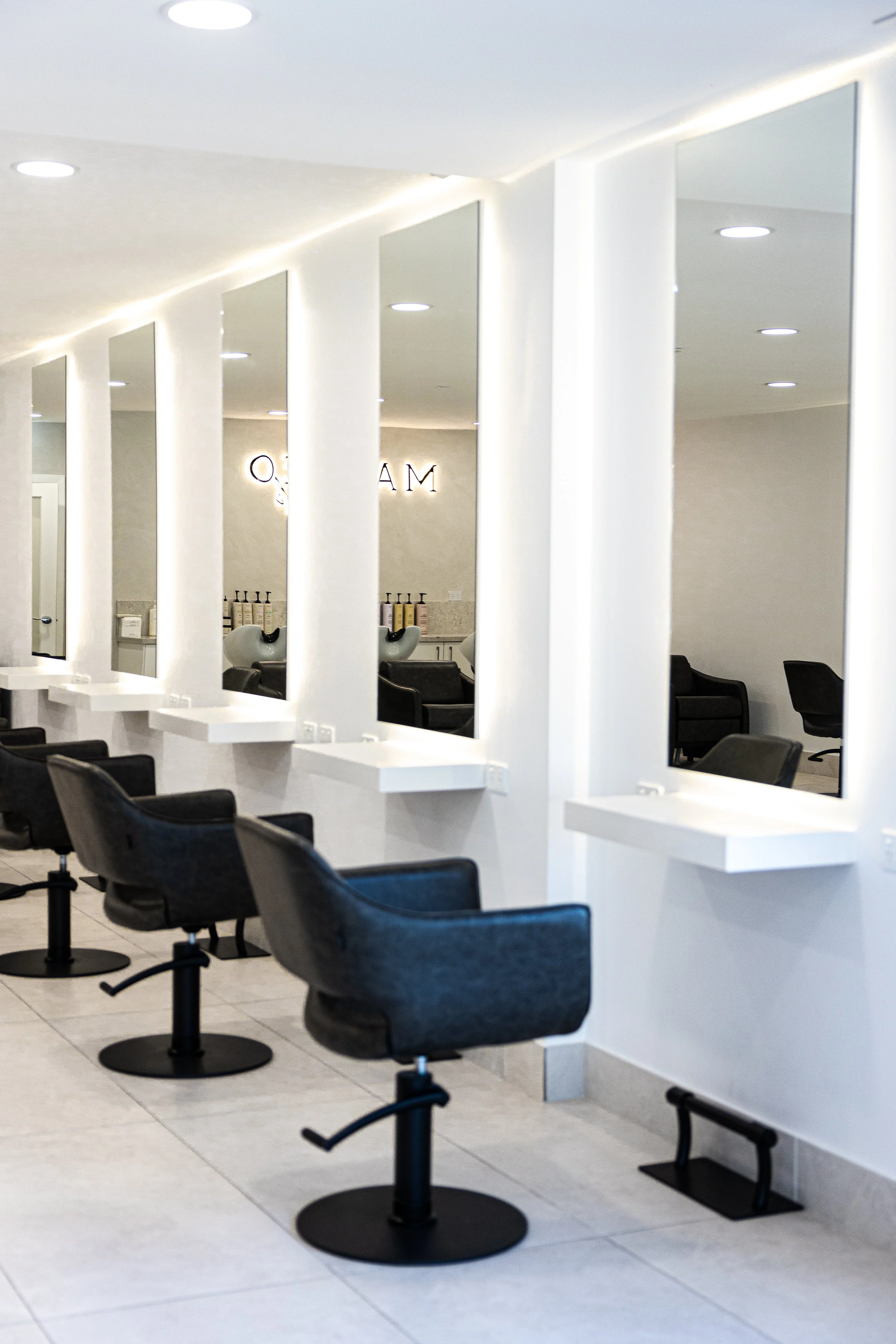 Modern salon with black styling chairs, white wall mirrors, and minimalistic decor.