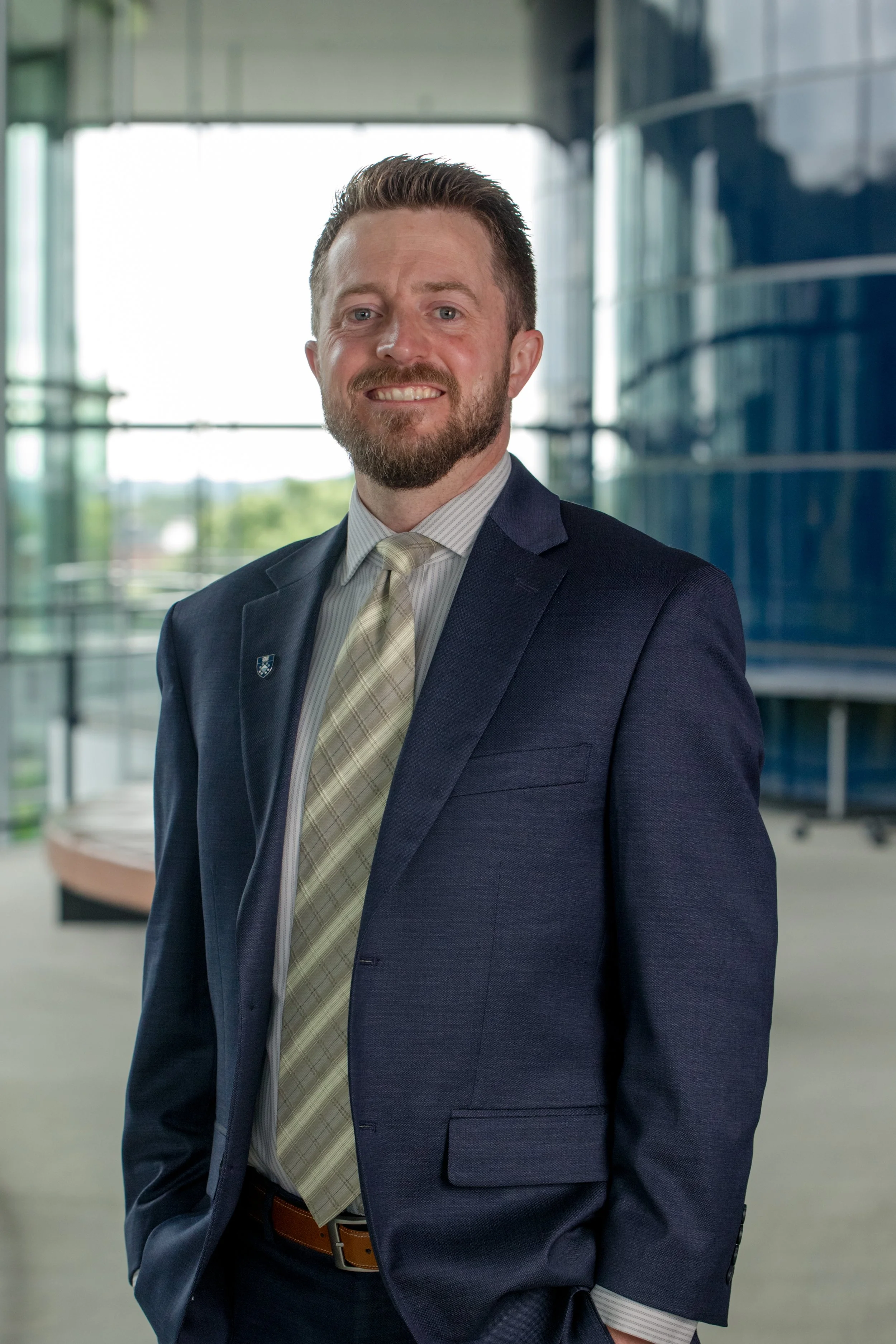 Blake Christensen in a business suit smiling, standing in a modern office building with large glass windows.