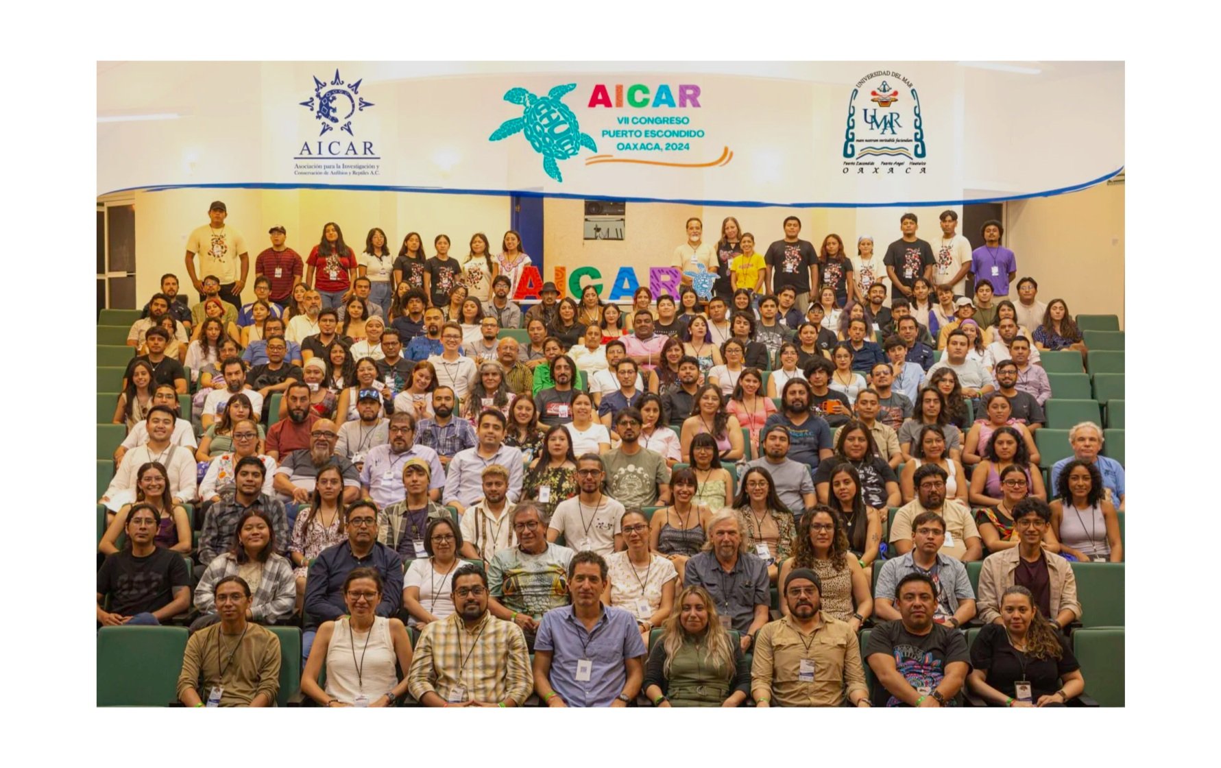 Grupo grande de personas en un auditorio durante un congreso, con carteles y logos de AICAR y UNI, todos posando para una fotografía grupal.