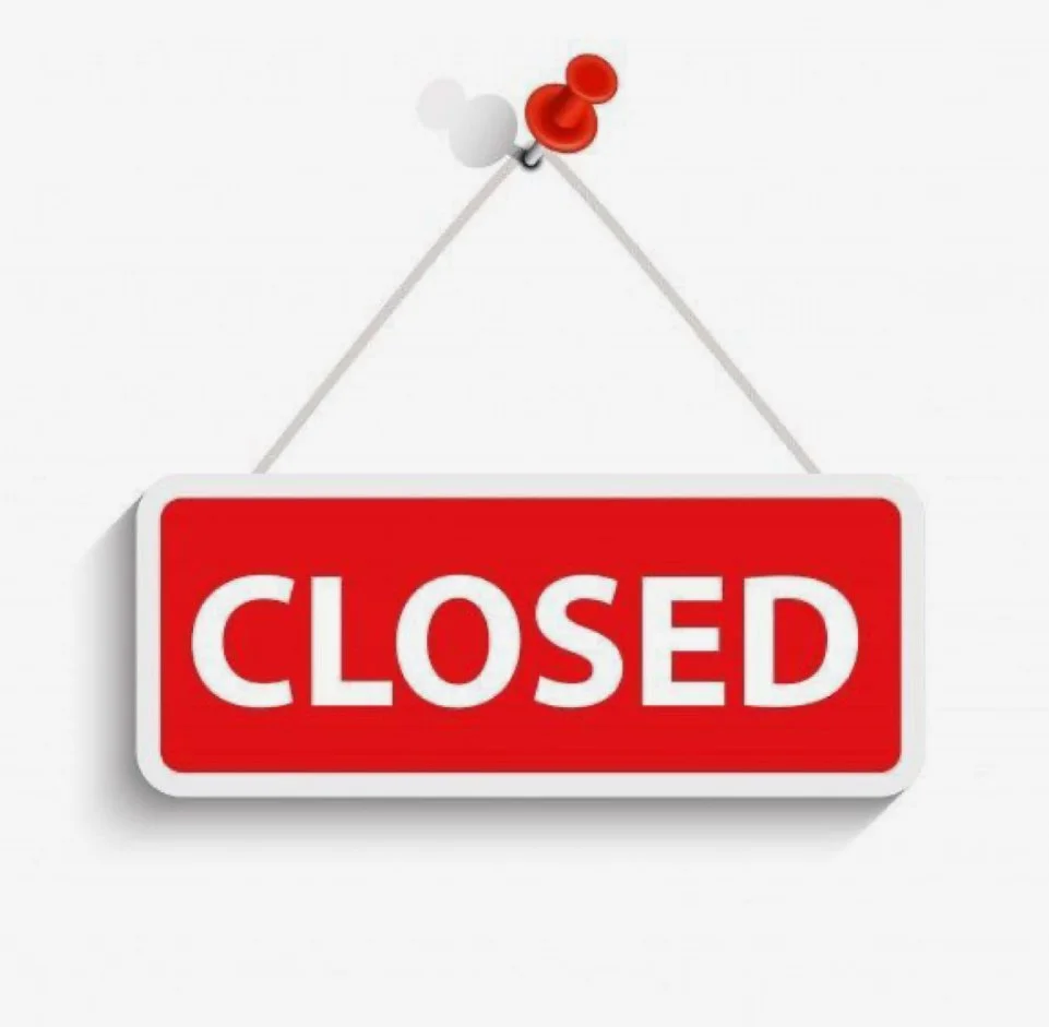 Red and white 'Closed' sign hanging by pins on a wall.