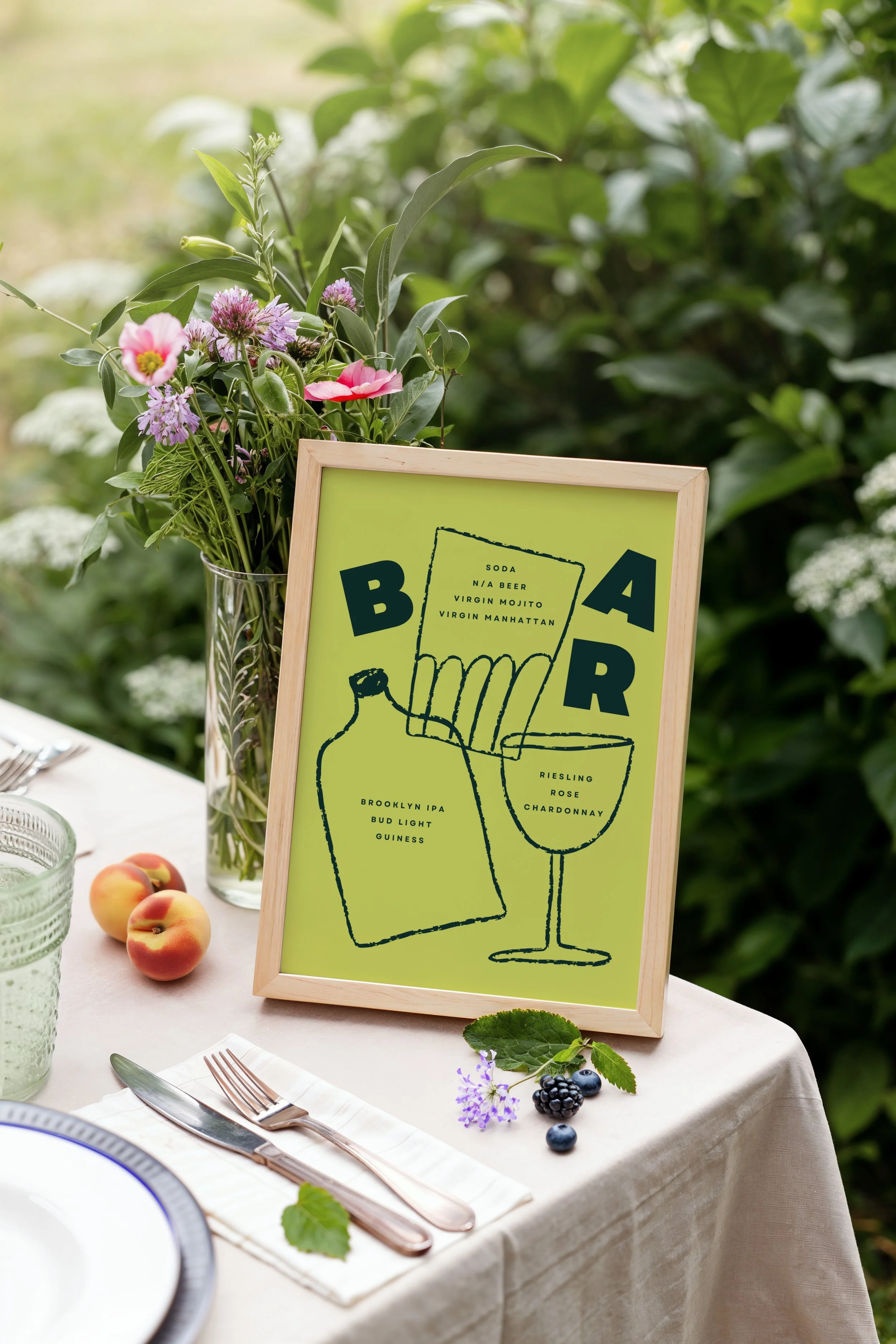 A table setting with a vase of flowers, peaches, a glass, a plate, silverware, and flowers on a tablecloth. A framed menu with a minimalist illustration of a drink and list of beverages stands on the table.