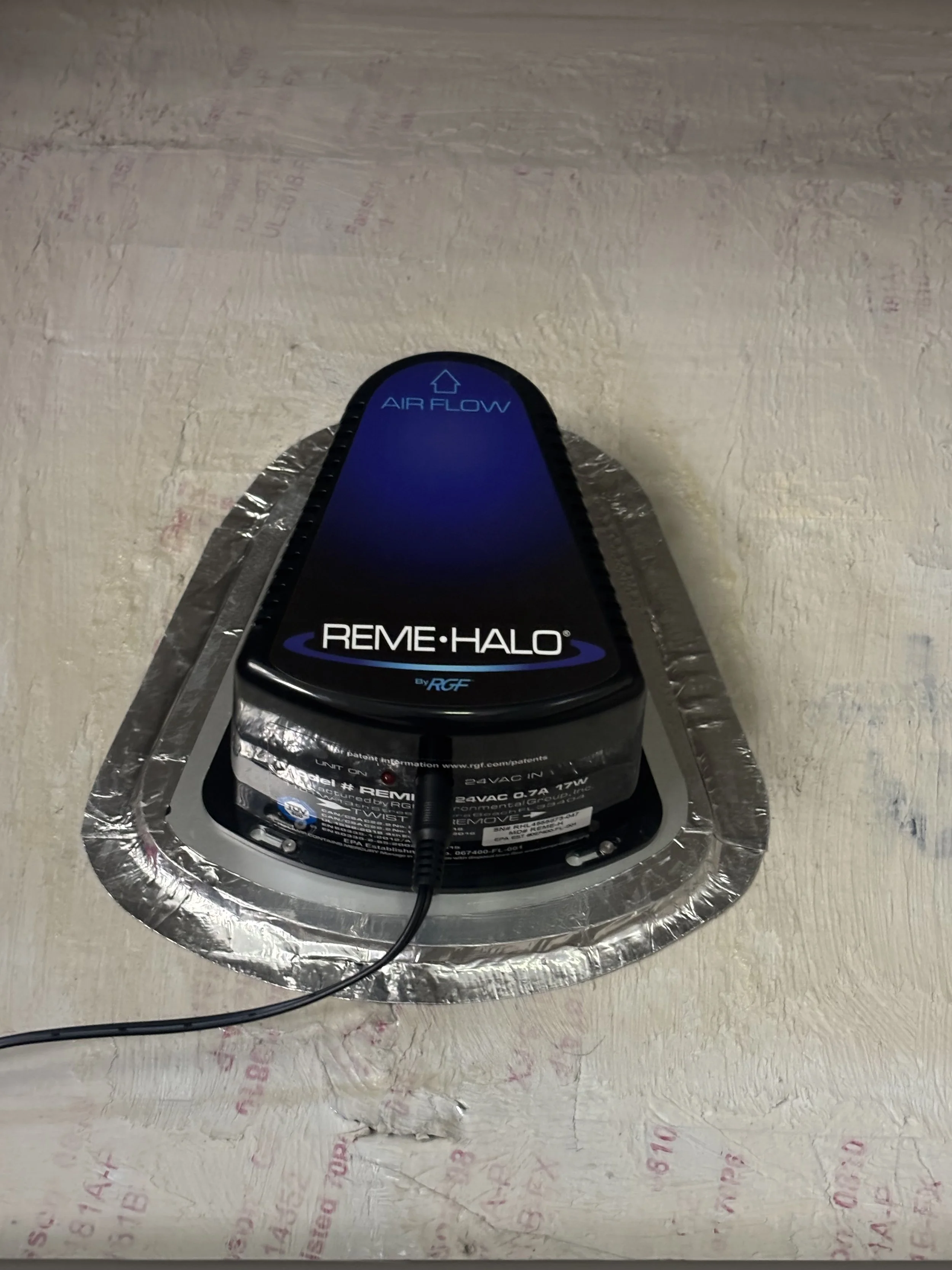 A medical device called REME HALO by RGF positioned on a ceiling with aluminum foil underneath, connected to a power source, with a label indicating 'AIR FLOW' and instructions.