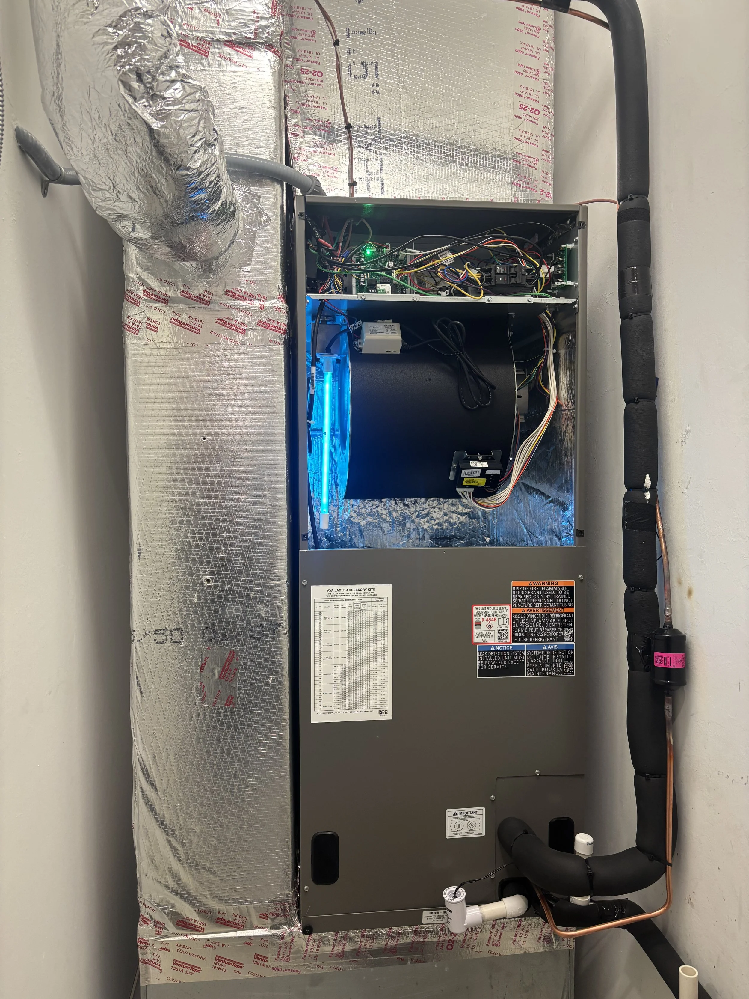 An HVAC unit with an exposed interior showing electrical wiring, a fan with blue light, and insulated ducts on the side.