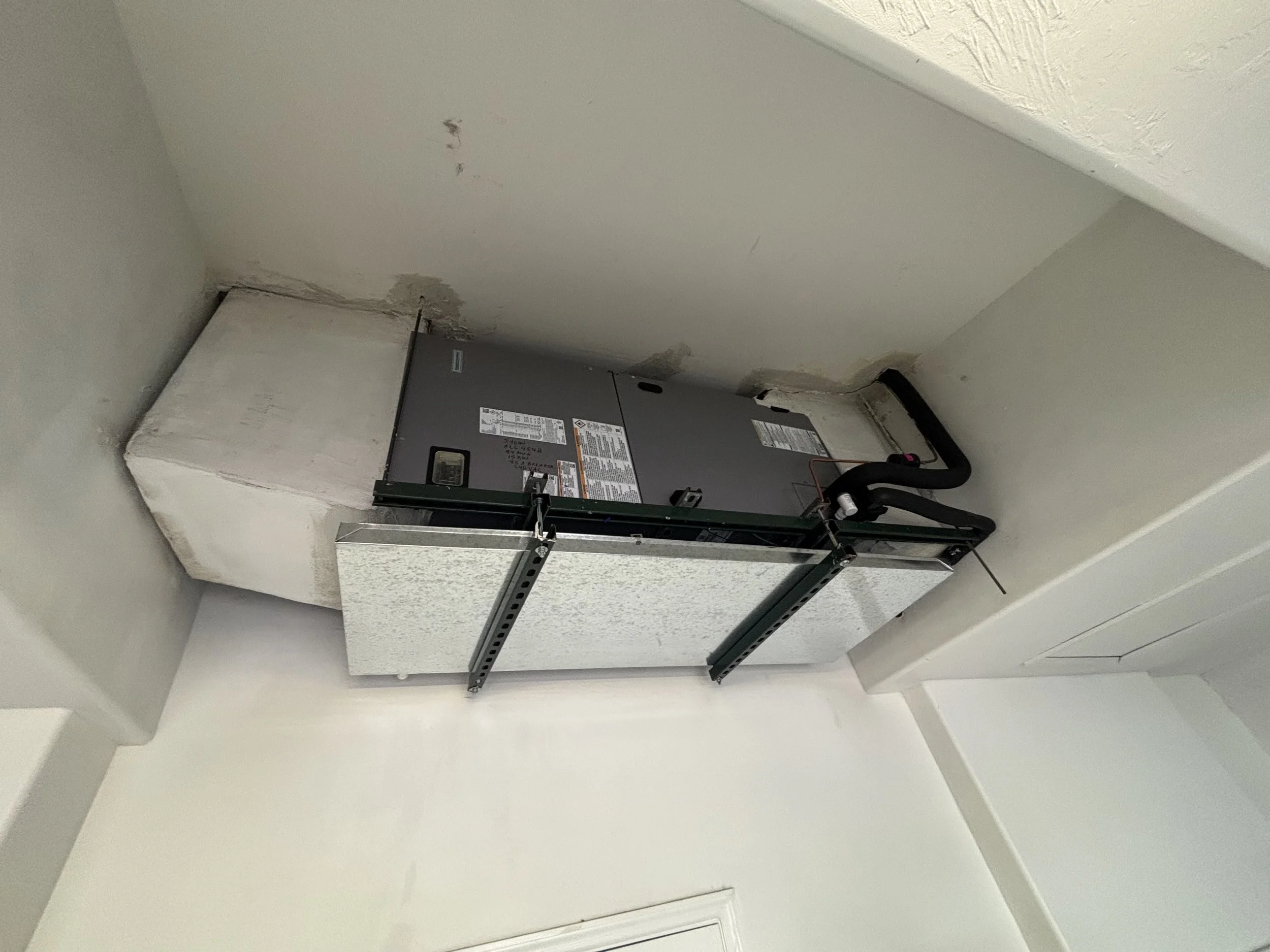 HVAC  unit installed in a ceiling cutout with visible pipes and ductwork