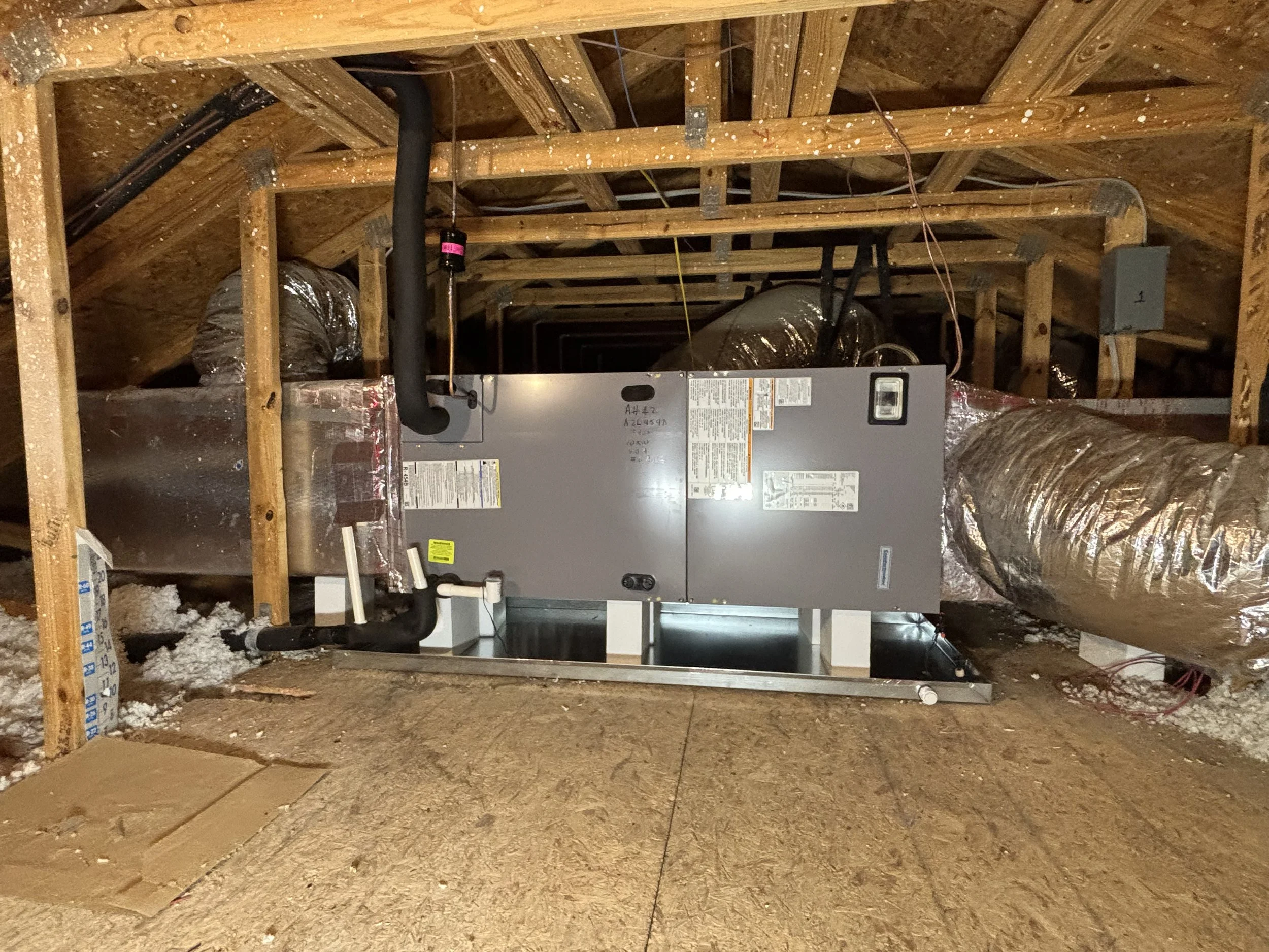 An HVAC air handler installed in an attic space with exposed wooden framing and ductwork.