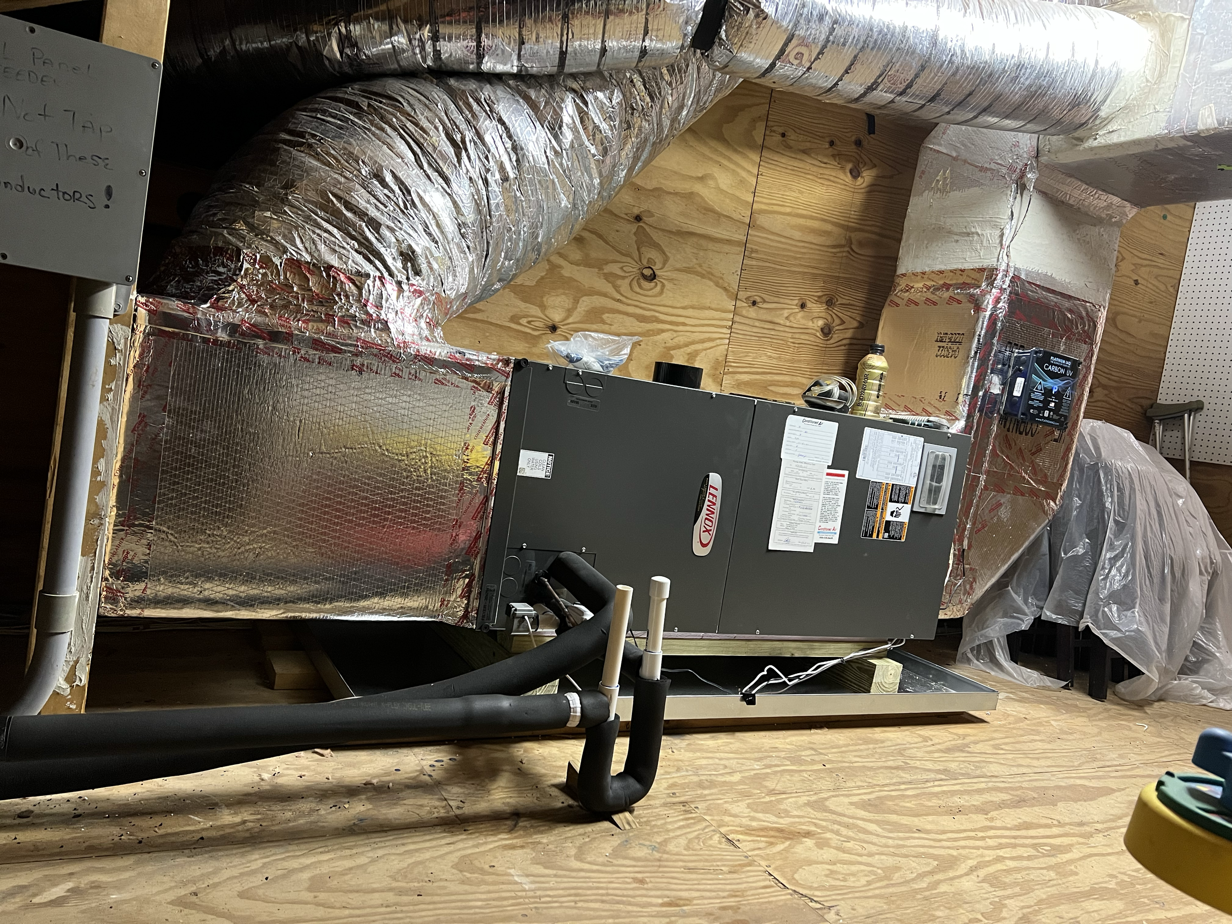 HVAC system with a Lennox air handler unit, insulated ductwork, and pipes in a utility room with wooden walls and floor.