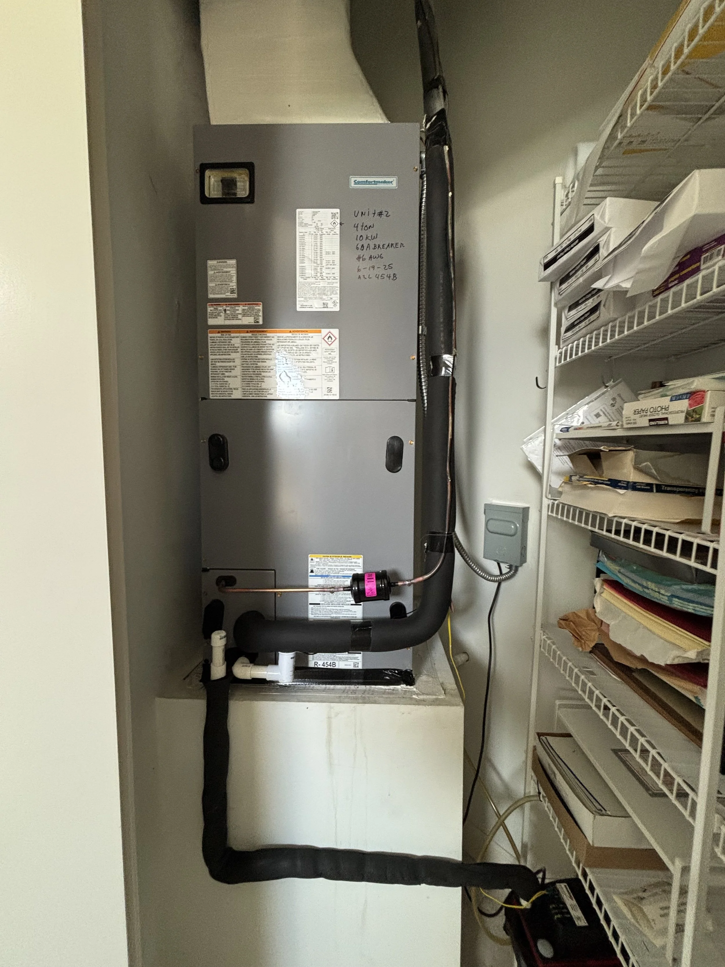 An HVAC unit installed in a closet with black insulated pipes and electrical wiring, surrounded by shelves with papers and documents.