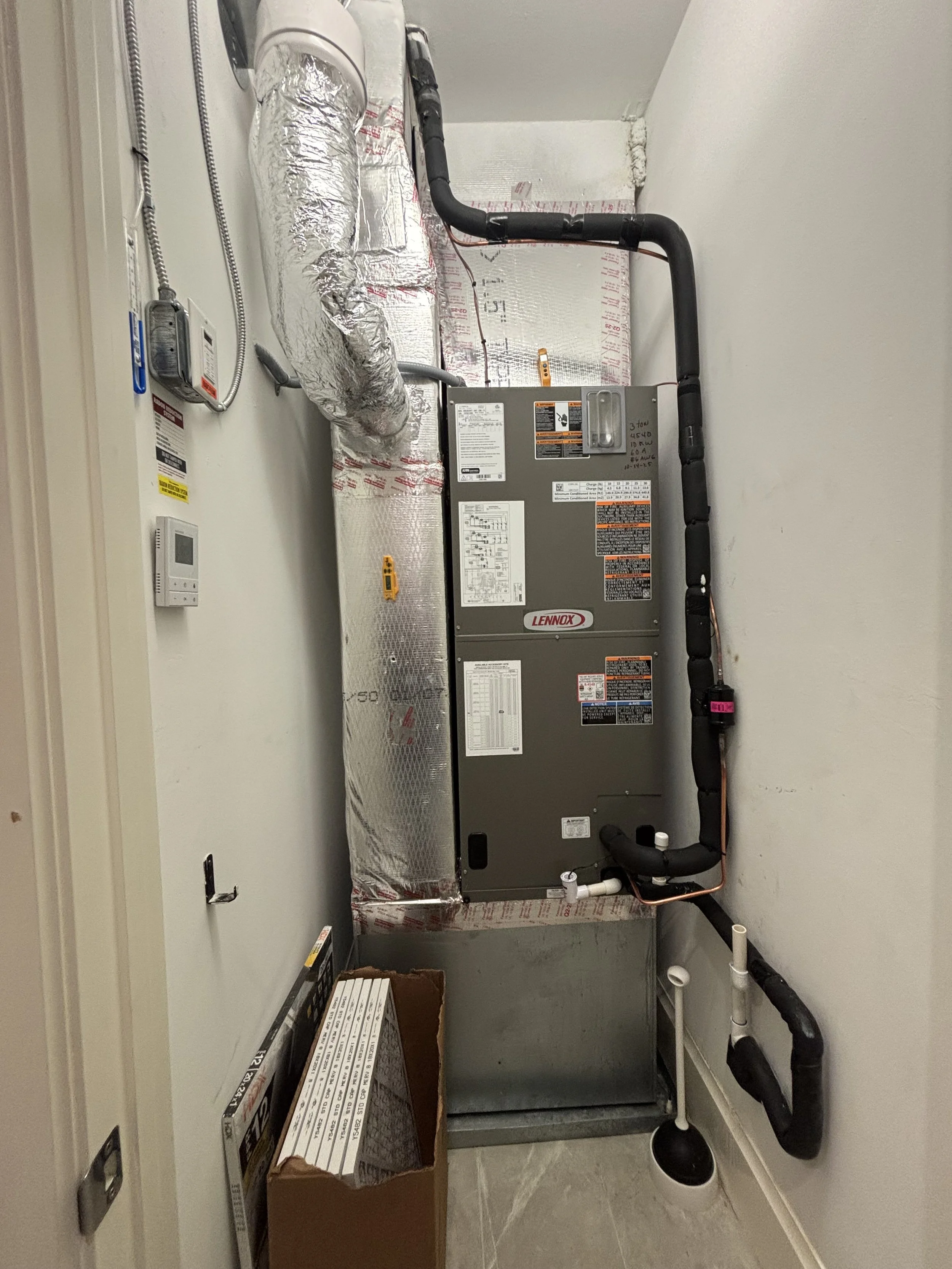 Installation of a new Lennox heating, ventilation, and air conditioning (HVAC) system in a utility closet, with black ductwork, insulated pipes, and tools on the floor.