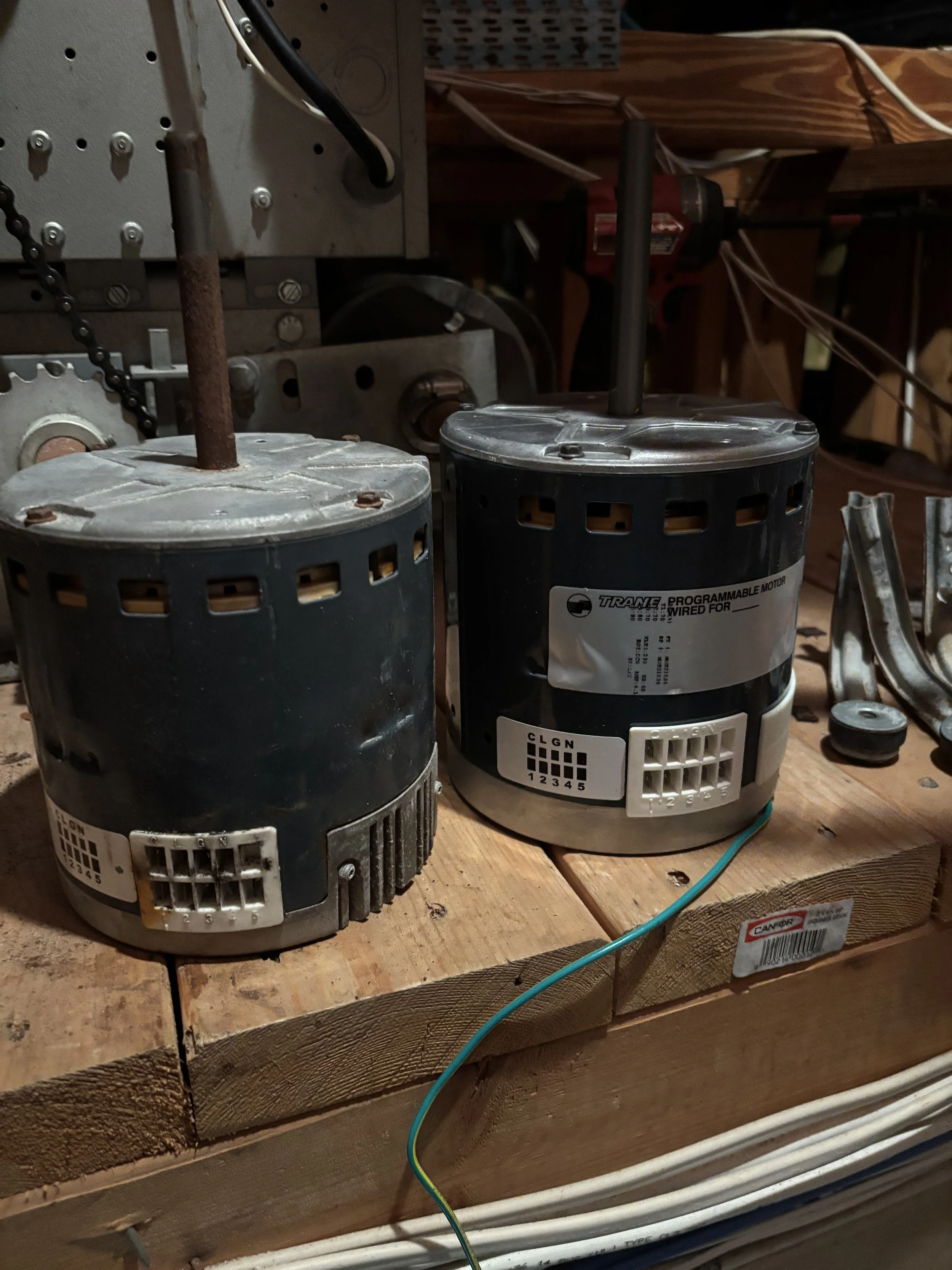 Two industrial motors mounted on a wooden workbench with various electrical wires and tools around.