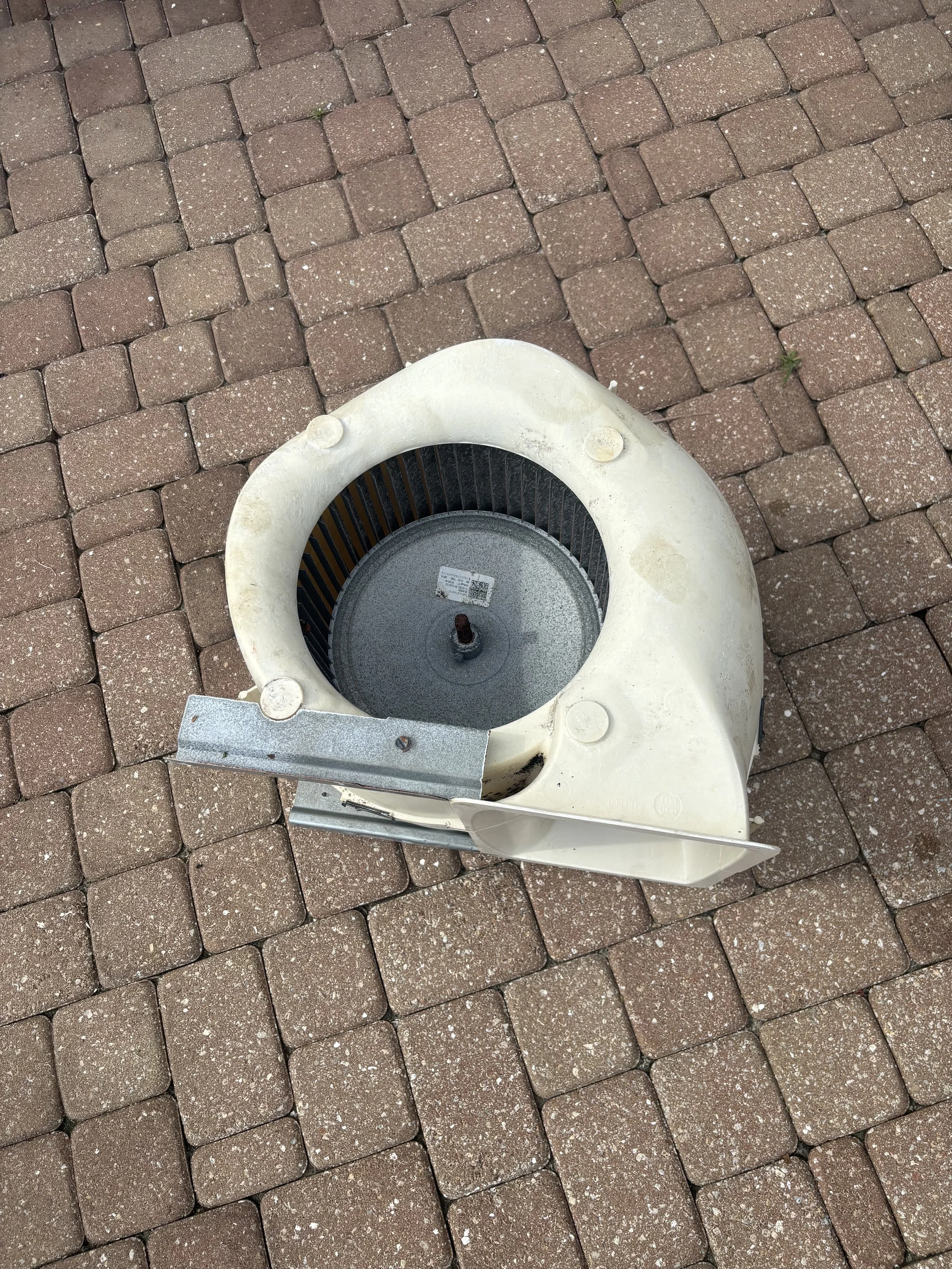An outdoor brick patio with a disassembled white ventilation fan or exhaust fan placed on it.