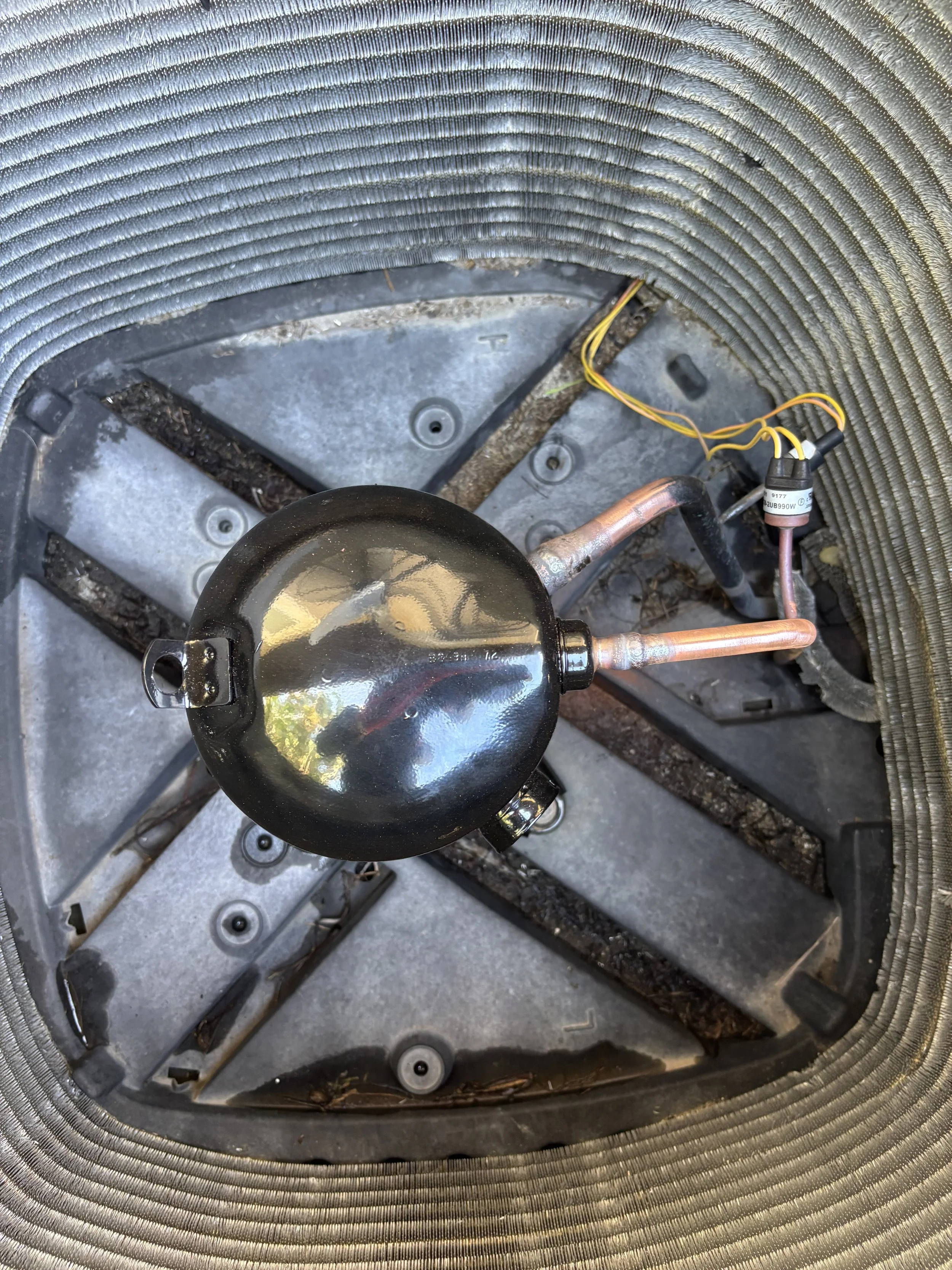 Image of the inside of an air conditioning unit, showing the compressor, copper pipes, electrical wires, and a fan guard.